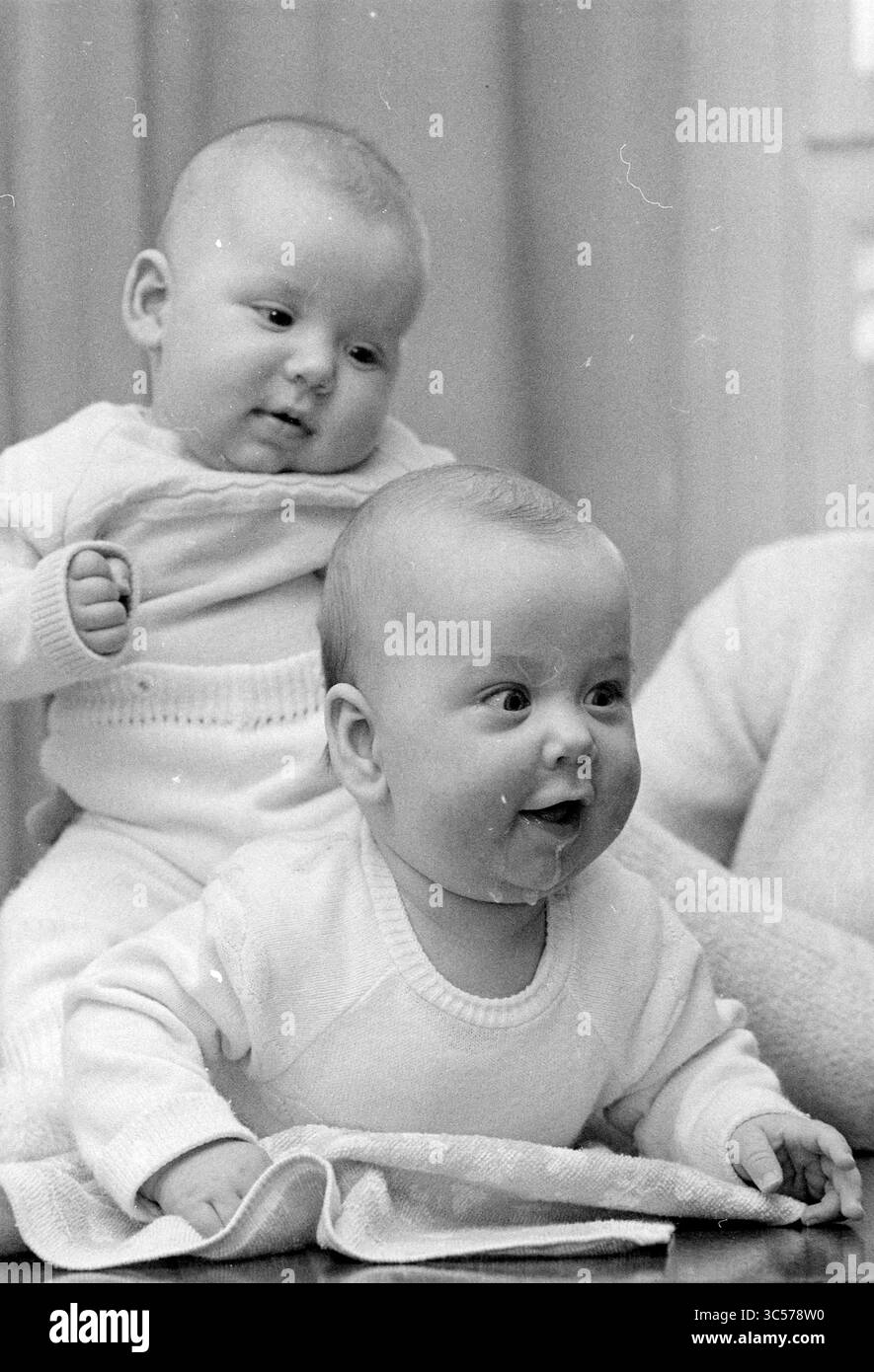 Twin, 00-00-1973 Whizgle News, Dutch Desk, Paesi Bassi, 1950-2000 due bambini che indossano maglioni a maglia coordinati si siedono insieme, uno che si piega in avanti con un'espressione gioiosa, mentre l'altro guarda curiosamente di lato. La scena cattura un momento di innocenza e giocosità. Foto Stock