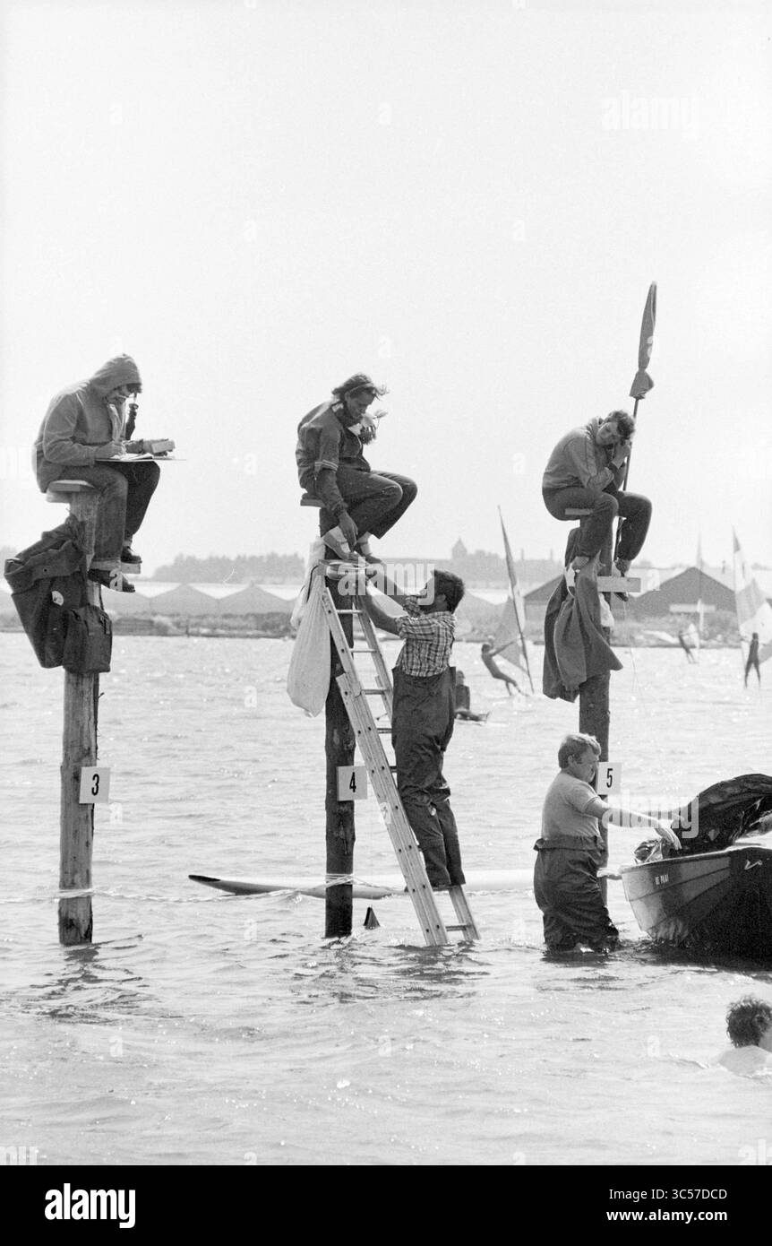 Concorso di pole sitting Oosterduinse Meer Noordwijkerhout, Noordwijkerhout, 00-00-1982 Whizgle News, Dutch Desk, Paesi Bassi, 1950-2000 Un gruppo di individui si impegna in varie attività nei pressi di un molo, con alcuni appollaiati su alti pali di legno, mentre altri lavorano su una barca nelle vicinanze, circondata dall'acqua e da barche a vela distanti. Foto Stock