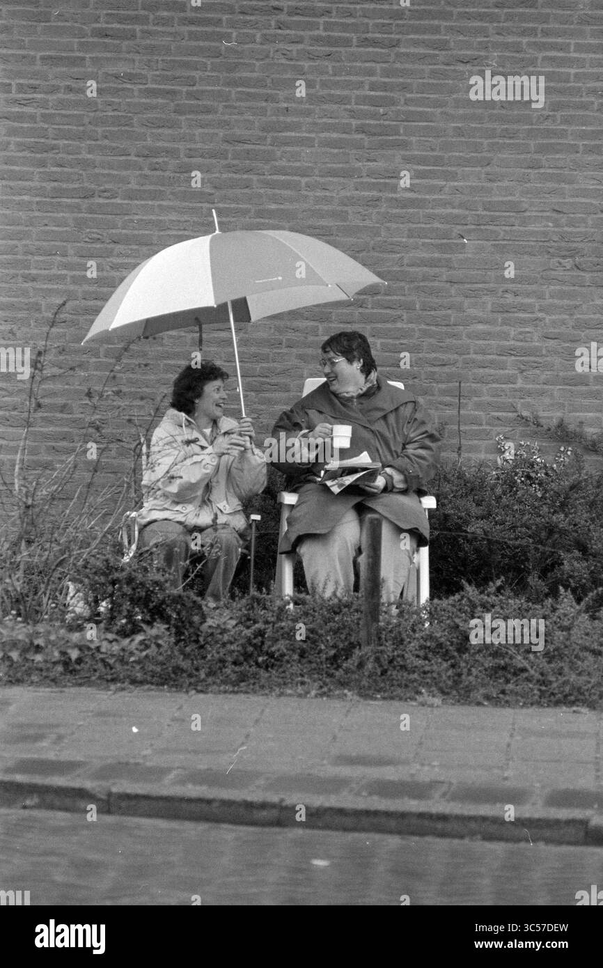 Traffic Exam, IJm., IJmuiden, Paesi Bassi, 26-04-1994 Whizgle News, Dutch Desk, Paesi Bassi, 1950-2000 due persone sedute su sedie sotto un ombrello colorato, impegnati in una conversazione mentre sorseggiano tazze di tè o caffè. Sono circondati da un giardino, che appare rilassato e contento in compagnia l'uno dell'altro. Foto Stock