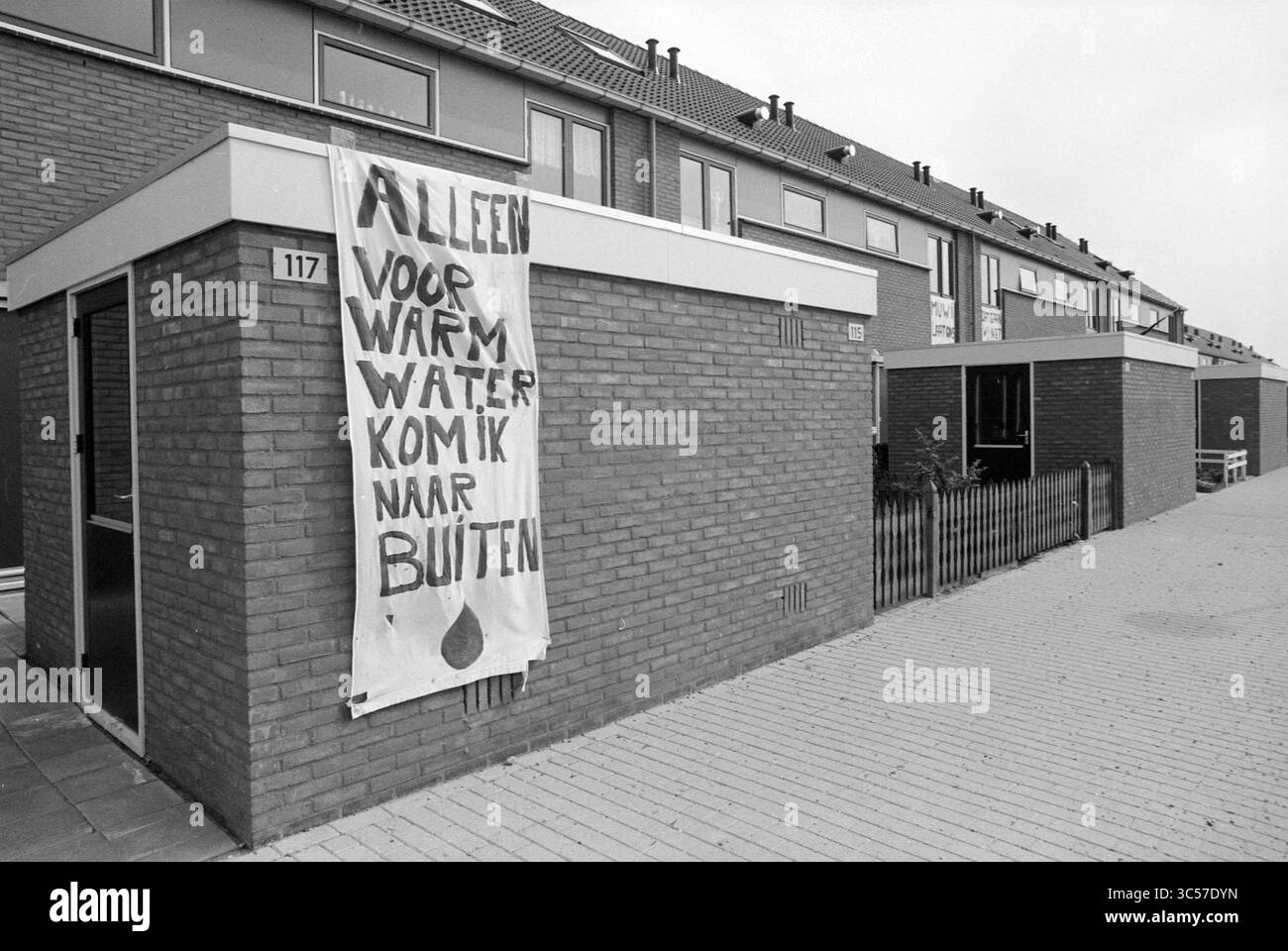2° membro del Parlamento nel distretto di Kalorama Hoofddorp, Hoofddorp, Paesi Bassi, 14-08-1987 Whizgle News, Dutch Desk, i Paesi Bassi, 1950-2000 Un grande striscione è appeso a un edificio, proclamando un messaggio che chiama le persone fuori per l'acqua calda. Le strutture circostanti sono semplici costruzioni in mattoni, con una modesta recinzione visibile nelle vicinanze, che creano una tranquilla scena urbana. Il cielo sopra è coperto, contribuendo a creare un'atmosfera soffusa. Foto Stock