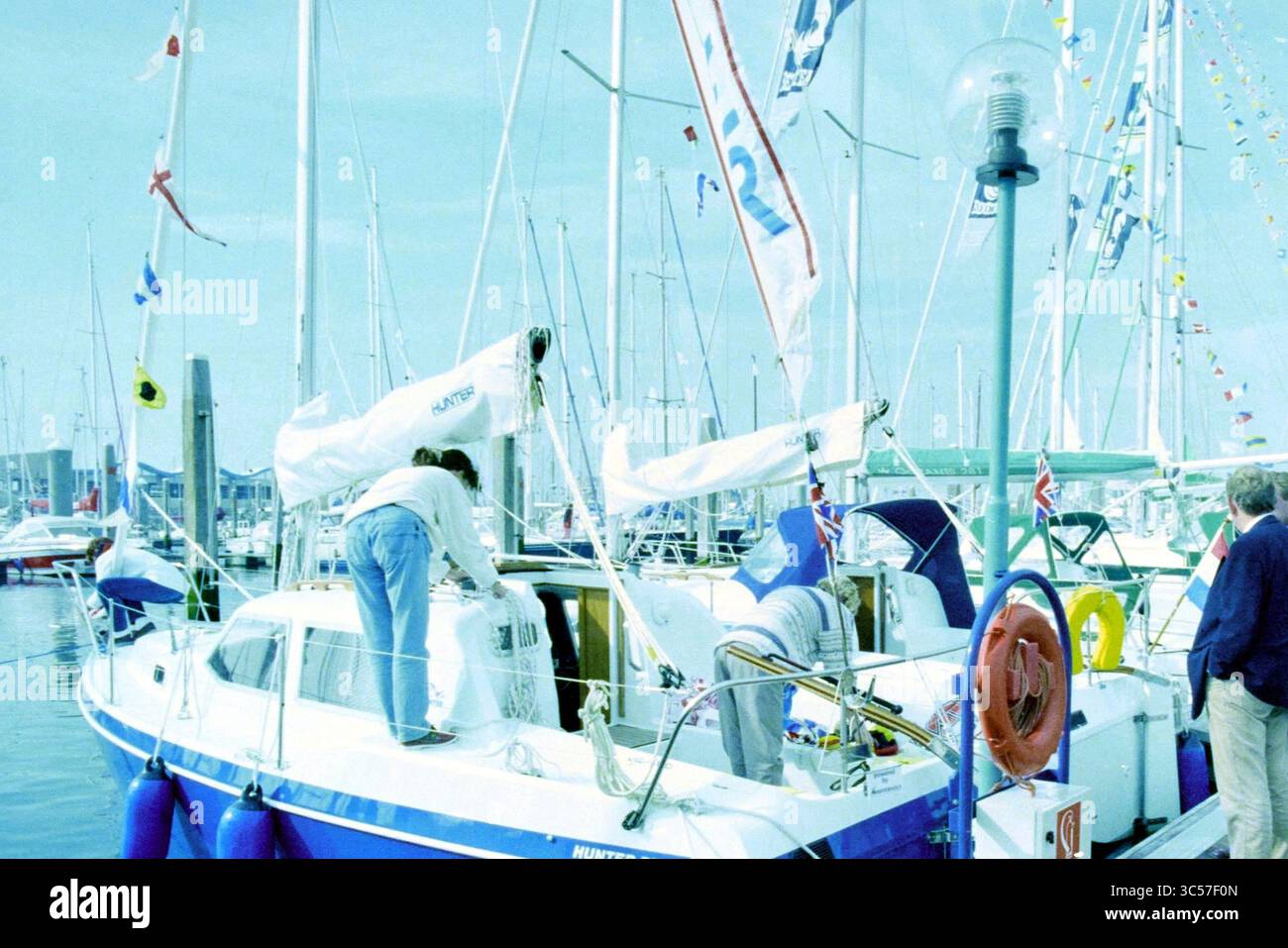 Hiswa te water, IJm., IJmuiden, Paesi Bassi, 04-09-1995 Whizgle News, Dutch Desk, Paesi Bassi, 1950-2000 due persone stanno preparando una barca a vela in un vivace porticciolo, con varie barche e bandiere colorate sullo sfondo. La scena cattura un senso di attività e di attesa mentre si preparano per una giornata sull'acqua. Foto Stock