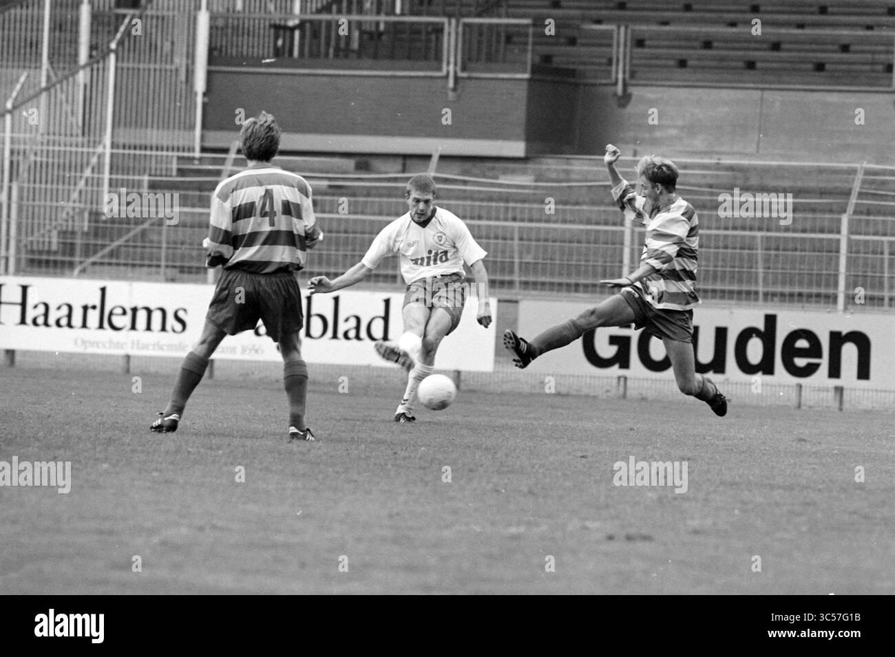 Football, Haarlem - Zandvoortmeeuwen, 24-09-1994 Whizgle News, Dutch Desk, Paesi Bassi, 1950-2000 Un giocatore di calcio con una maglia leggera colpisce abilmente la palla mentre due giocatori avversari, indossando maglie a strisce, reagiscono nel tentativo di intercettare il gioco. I posti a sedere a stadio sono visibili sullo sfondo, sottolineando l'atmosfera competitiva della partita. Foto Stock