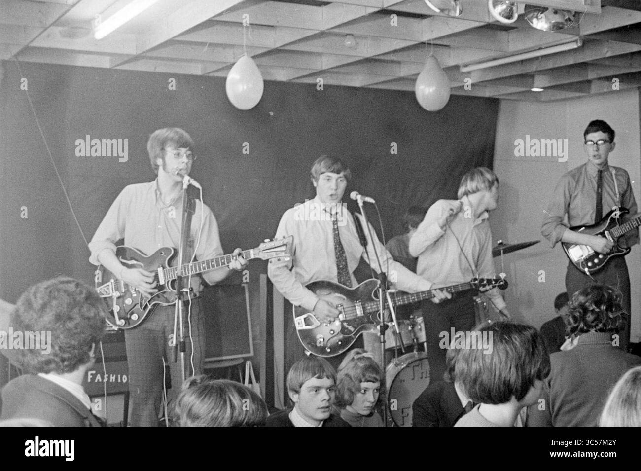 Gruppo beat: The New Fashion sul palco Whizgle News, Dutch Desk, Paesi Bassi, 1950-2000 Una band vivace si esibisce sul palco mentre gli spettatori entusiasti si divertono. I musicisti, vestiti con magliette e cravatte, suonano abilmente le chitarre mentre un membro canta nel microfono. Palloncini colorati fluttuano sopra la folla, aggiungendo un'atmosfera energetica all'evento. Foto Stock