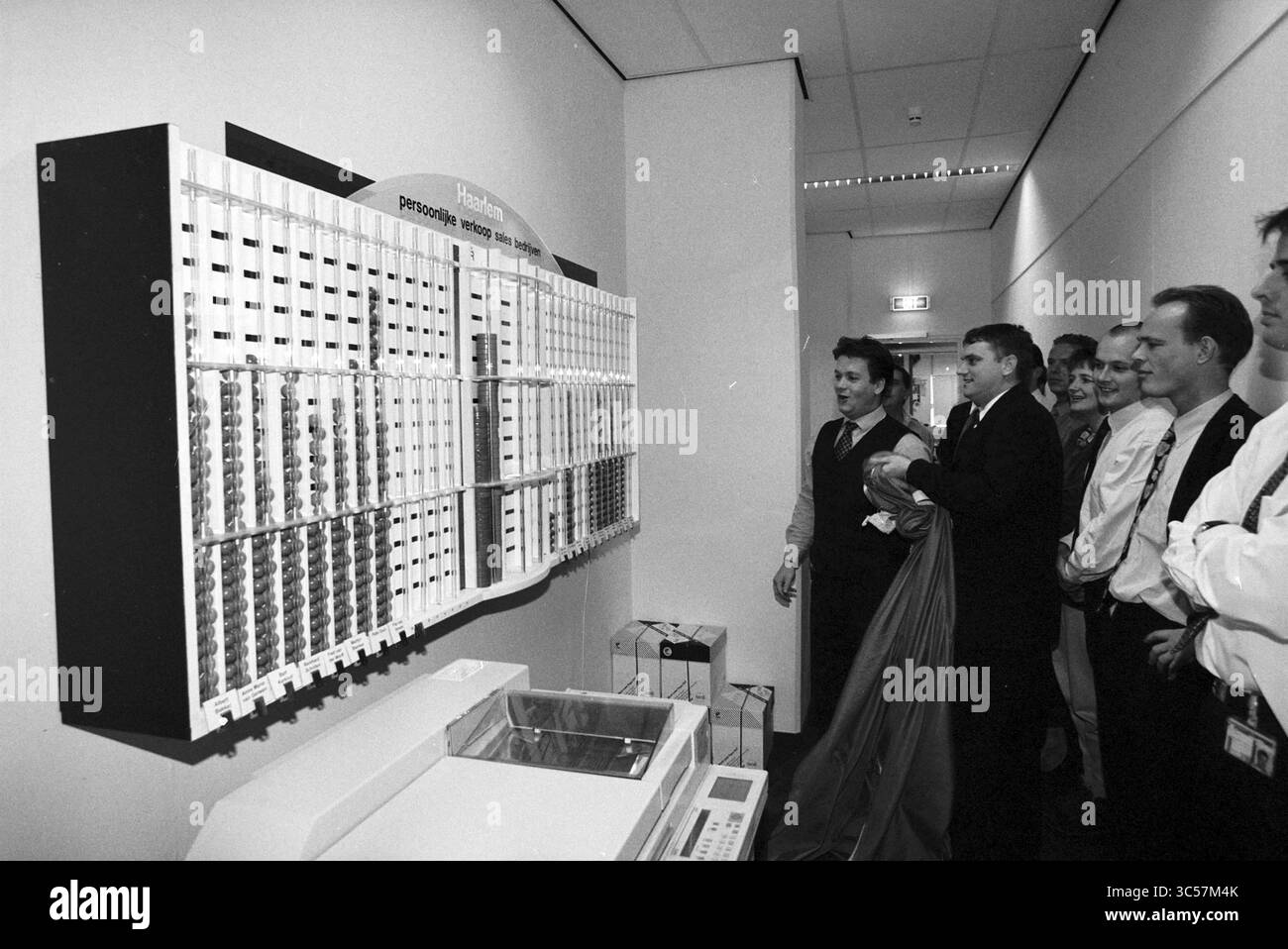 Presentazione del comitato di pianificazione Waarderpolder, Haarlem, Paesi Bassi, 24-11-1997 Whizgle News, Dutch Desk, i Paesi Bassi, 1950-2000 Un gruppo di individui si riunisce intorno a un grande display con una serie di slot organizzati, presumibilmente contenenti informazioni. Alcuni partecipanti sembrano impegnati, mentre una persona si prepara a svelare o presentare qualcosa, aggiungendo un elemento di anticipazione alla scena. Foto Stock