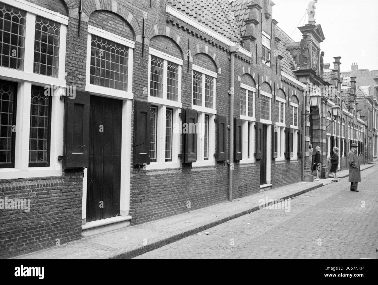 Cortile e esterno del Frans H.Museum, Frans Hals Museum, 16-10-1961 Whizgle News, Dutch Desk, Paesi Bassi, 1950-2000 Una stretta strada acciottolata fiancheggiata da edifici storici in mattoni caratterizzati da finestre ad arco e porte in legno. Due persone sono viste conversare vicino all'ingresso di uno degli edifici, mentre l'architettura mostra elementi di design tradizionali olandesi. Foto Stock