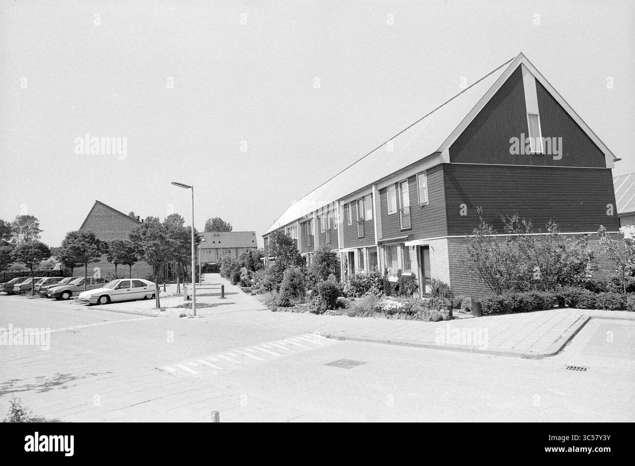 Strada residenziale con blocchi di case, 00-05-1989 Whizgle News, Dutch Desk, The Netherlands, 1950-2000 Una fila di case moderne presenta distinti tetti inclinati e giardini ben tenuti, adagiati su uno sfondo di alberi e edifici vicini. Un'area parcheggio mette in mostra diverse auto, sottolineando l'atmosfera suburbana della comunità. Foto Stock