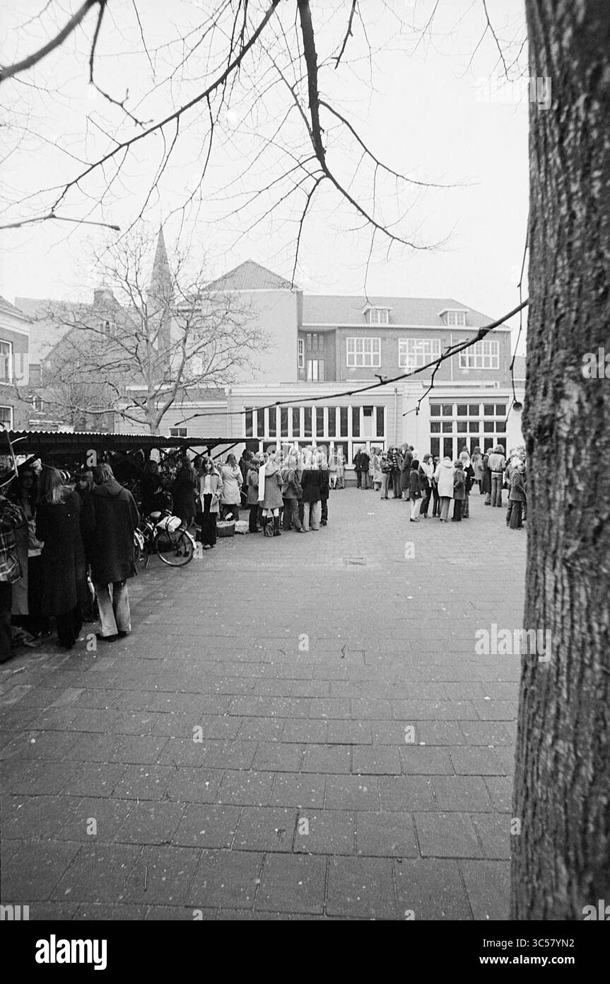 Studenti sul cortile scolastico, 00-00-1972 Whizgle News, Dutch Desk, Paesi Bassi, 1950-2000 Una vivace piazza piena di gruppi di persone riuniti intorno a varie bancarelle, con edifici e una guglia della chiesa sullo sfondo. Gli alberi sono al limite e l'atmosfera suggerisce un evento o un giorno di mercato. Foto Stock
