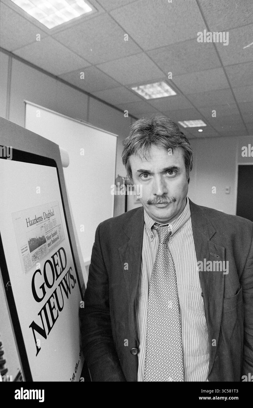 Presentazione della campagna promozionale Leidsch Dagblad e Haarlems Dagblad., 01-07-1992 Whizgle News, Dutch Desk, Paesi Bassi, 1950-2000 Un uomo in abbigliamento formale si erge accanto a un display con il titolo "GOED NIEUWS", con un titolo di giornale visibile. L'impostazione sembra essere un ufficio, con uno sfondo neutro e un'illuminazione soffusa. Foto Stock