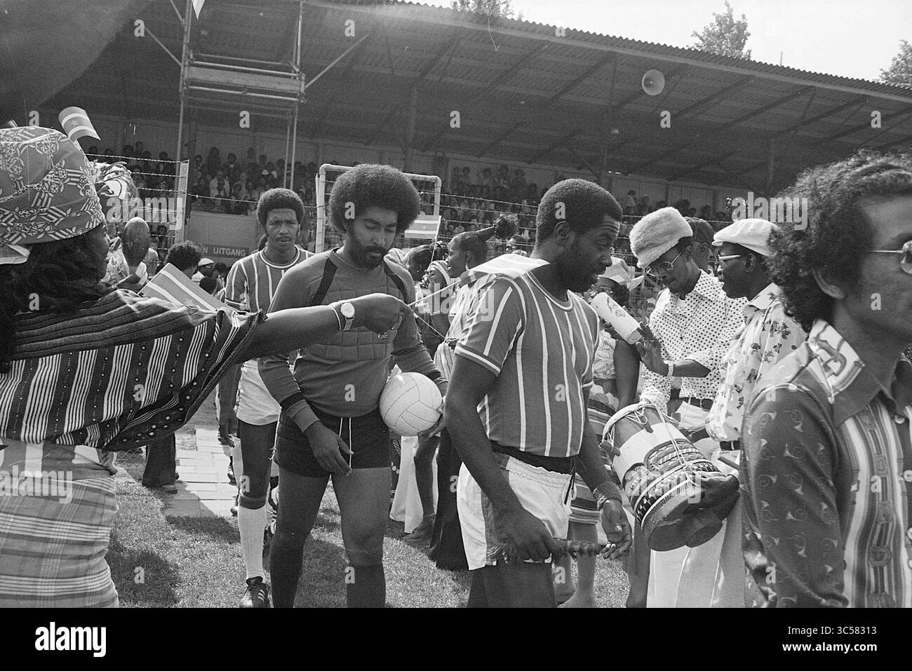 Haarlem - Robin Hood, Football Haarlem, 15-08-1976 Whizgle News, Dutch Desk, Paesi Bassi, 1950-2000 Un gruppo di uomini in un abbigliamento colorato, con motivi vivaci e cappelli, si riuniscono sul campo, con uno che tiene una partita di calcio. Sembrano far parte di un team o di un evento, mostrando un'atmosfera vivace piena di attesa ed entusiasmo. Le tribune circostanti sono piene di spettatori, a indicare un'occasione celebrativa o competitiva. Foto Stock