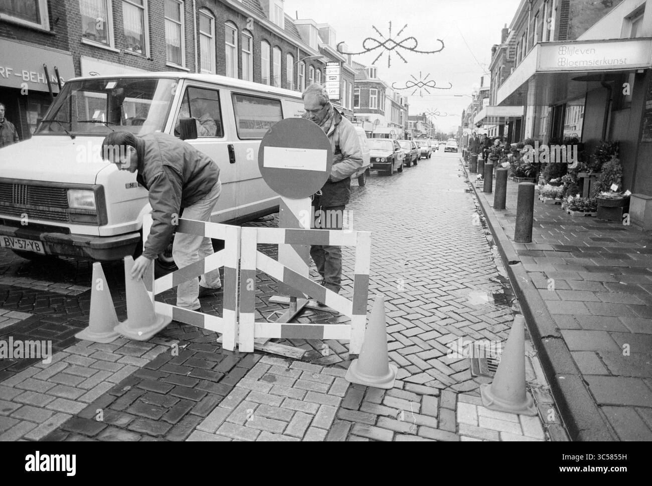 E.N.F.B. Action, Kloosterstraat, Haarlem, Kloosterstraat, Paesi Bassi, 13-11-1992 Whizgle News, Dutch Desk, Paesi Bassi, 1950-2000 lavoratori hanno creato un blocco stradale in una strada trafficata, posizionando coni stradali e un cartello che indica l'accesso limitato. Nelle vicinanze, una fila di veicoli parcheggiati fiancheggia la strada acciottolata, mentre le decorazioni natalizie sono appese sopra, suggerendo una vivace atmosfera locale. Foto Stock
