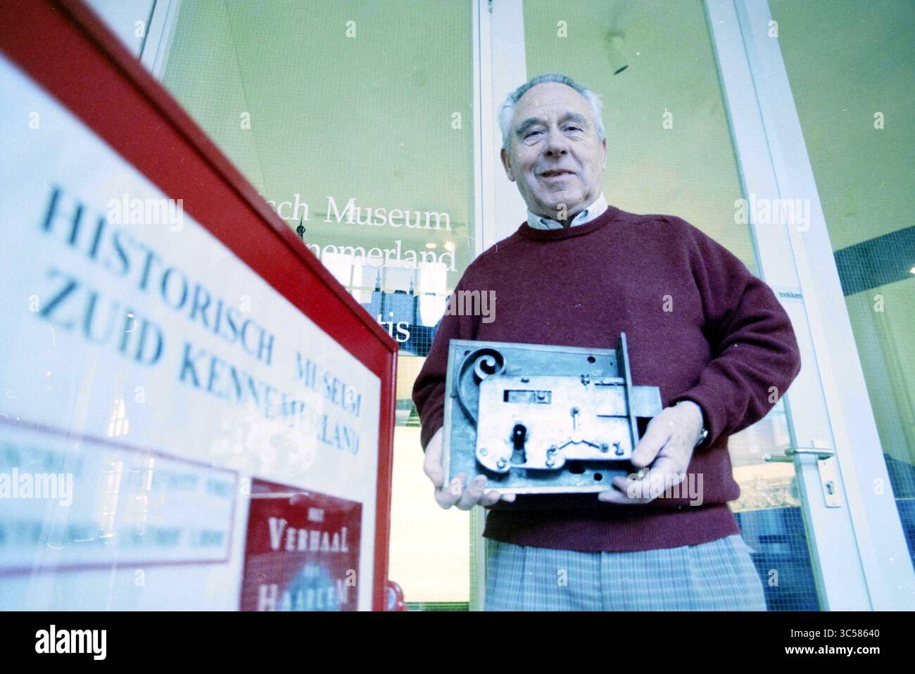 Marcel Brenneraedts ha una mostra della sua collezione di serrature e chiavi nel Museo storico Zuid-Kennemerland sotto il titolo "chiuse storiche"., Haarlem, Groot Heiligland, Paesi Bassi, 20-02-1996 Whizgle News, Dutch Desk, Paesi Bassi, 1950-2000 un anziano si erge orgogliosamente all'esterno di un museo, con un meccanismo anticato progettato in modo complesso. È vestito con un maglione e pantaloni a scacchi, trasuda un senso di nostalgia e orgoglio nel condividere un pezzo di storia. Dietro di lui, l'ingresso del museo è visibile, indicando il significato dell'artefatto nel contesto dell'heritag locale Foto Stock