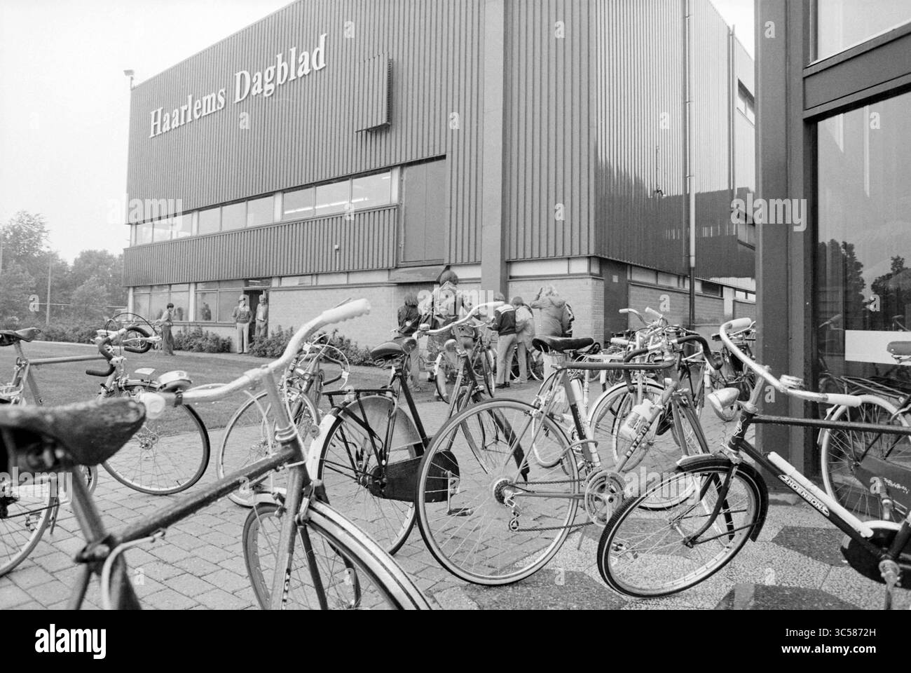 Ispezione biciclette Mosquito Round, Mosquito Round, 01-08-1979 Whizgle News, Dutch Desk, Paesi Bassi, 1950-2000 biciclette sono parcheggiate di fronte a un edificio moderno, con persone riunite nelle vicinanze, probabilmente impegnate in varie attività legate allo stabilimento. La scena cattura un momento di vita urbana, mescolando trasporti e interazione con la comunità. Foto Stock