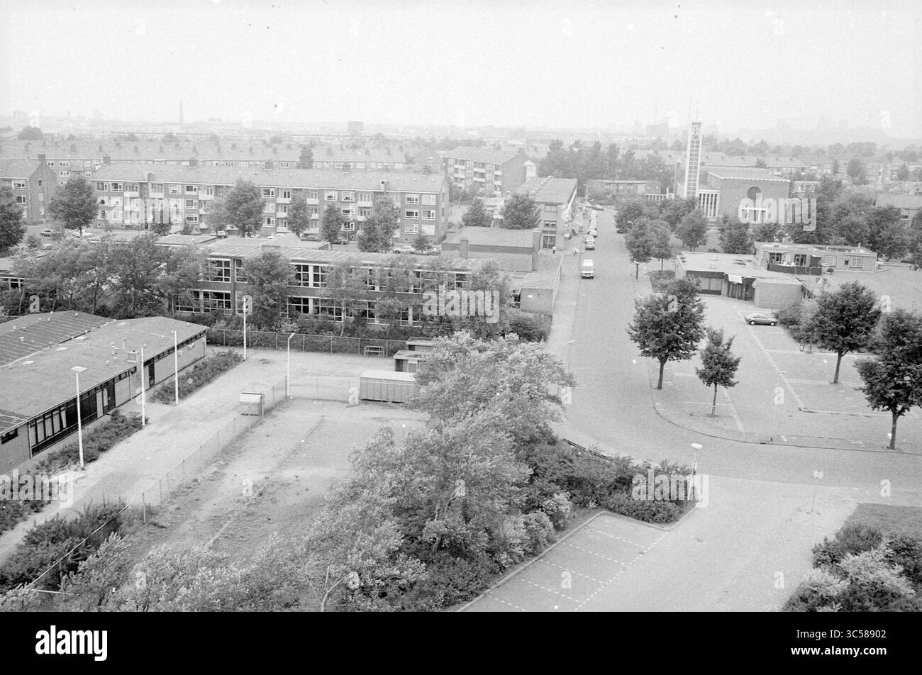 Palazzetto dello sport e campi da calcio Zeewijk, IJmuiden, The Netherlands Whizgle News, Dutch Desk, The Netherlands, 1950-2000 Un'ampia vista di un'area suburbana con file di edifici residenziali, alberi sparsi e una chiesa in lontananza. Le strade attraversano il quartiere, con auto parcheggiate e spazi vuoti che indicano un'atmosfera tranquilla. Il paesaggio è caratterizzato da un mix di struttura urbana e vegetazione. Foto Stock