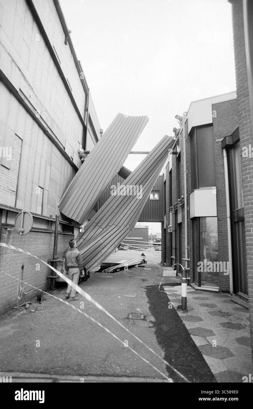 Storm Damage various, Haarlem, Storm and Storm Damage, Haarlem, Nederland, 26-01-1990 Whizgle News, Dutch Desk, i Paesi Bassi, 1950-2000 Un lavoratore si trova accanto a grandi lamiere piegate che sono crollate tra due edifici, creando una scena caotica in un vicolo. Le strutture circostanti mostrano un mix di texture e materiali, sottolineando l'impatto dei detriti caduti. Foto Stock
