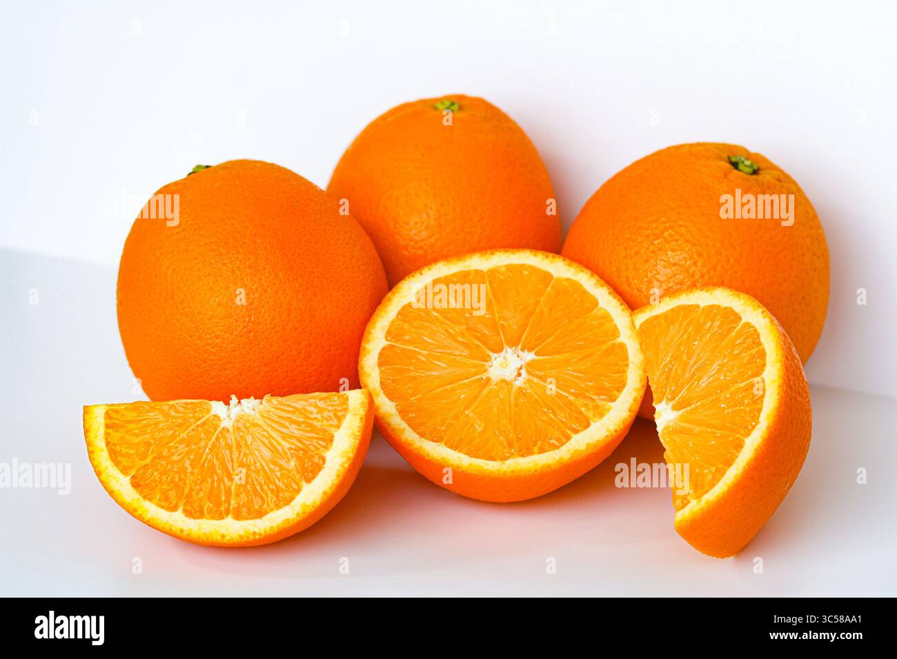 Vivaci arance sunkiste. Tre interi, uno a metà e due fette, catturati con una luce nitida su uno sfondo bianco. Foto Stock