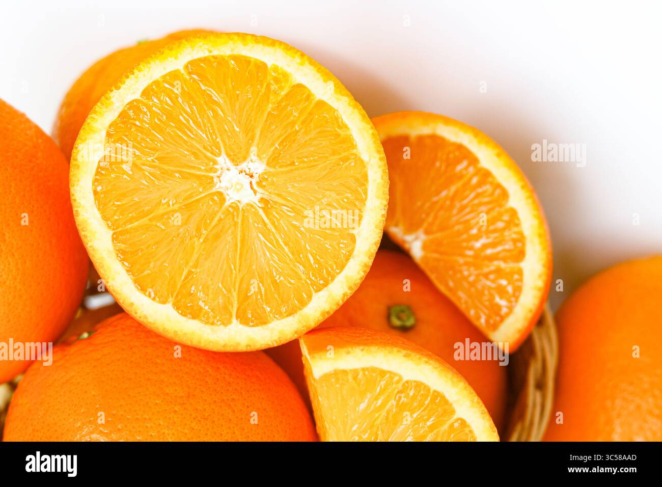 Primo piano di arance mature sunkist, intere e tagliate, immerse in un cestino intrecciato. Un ambiente vivace con frutta. Foto Stock