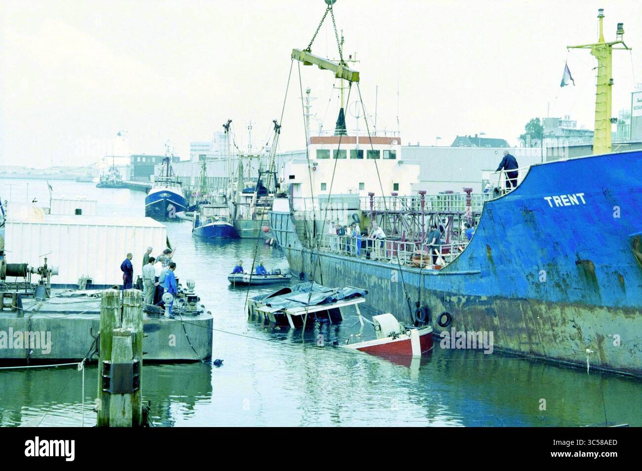 Boat Raised, IJmuiden, IJmuiden, Paesi Bassi, 07-09-1999 Whizgle News, Dutch Desk, Paesi Bassi, 1950-2000 Una vivace scena portuale presenta barche da pesca e navi più grandi attraccate lungo la banchina. I lavoratori sono visti impegnati in varie attività vicino all'acqua, mentre le barche più piccole sono ormeggiate nelle vicinanze. L'atmosfera suggerisce un vivace ambiente portuale, con edifici che fiancheggiano la riva sullo sfondo. Foto Stock