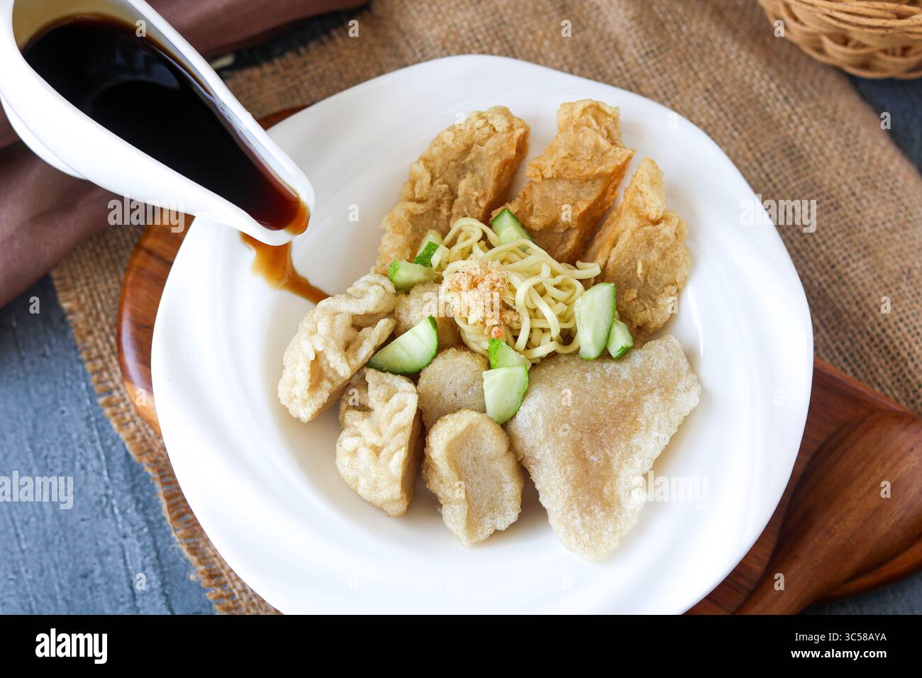 Versare salsa cuko scura su un piatto ammassato con un assortimento di Pempek (o Empek-Empek), un tradizionale piatto di torta di pesce indonesiano di Palembang. Foto Stock