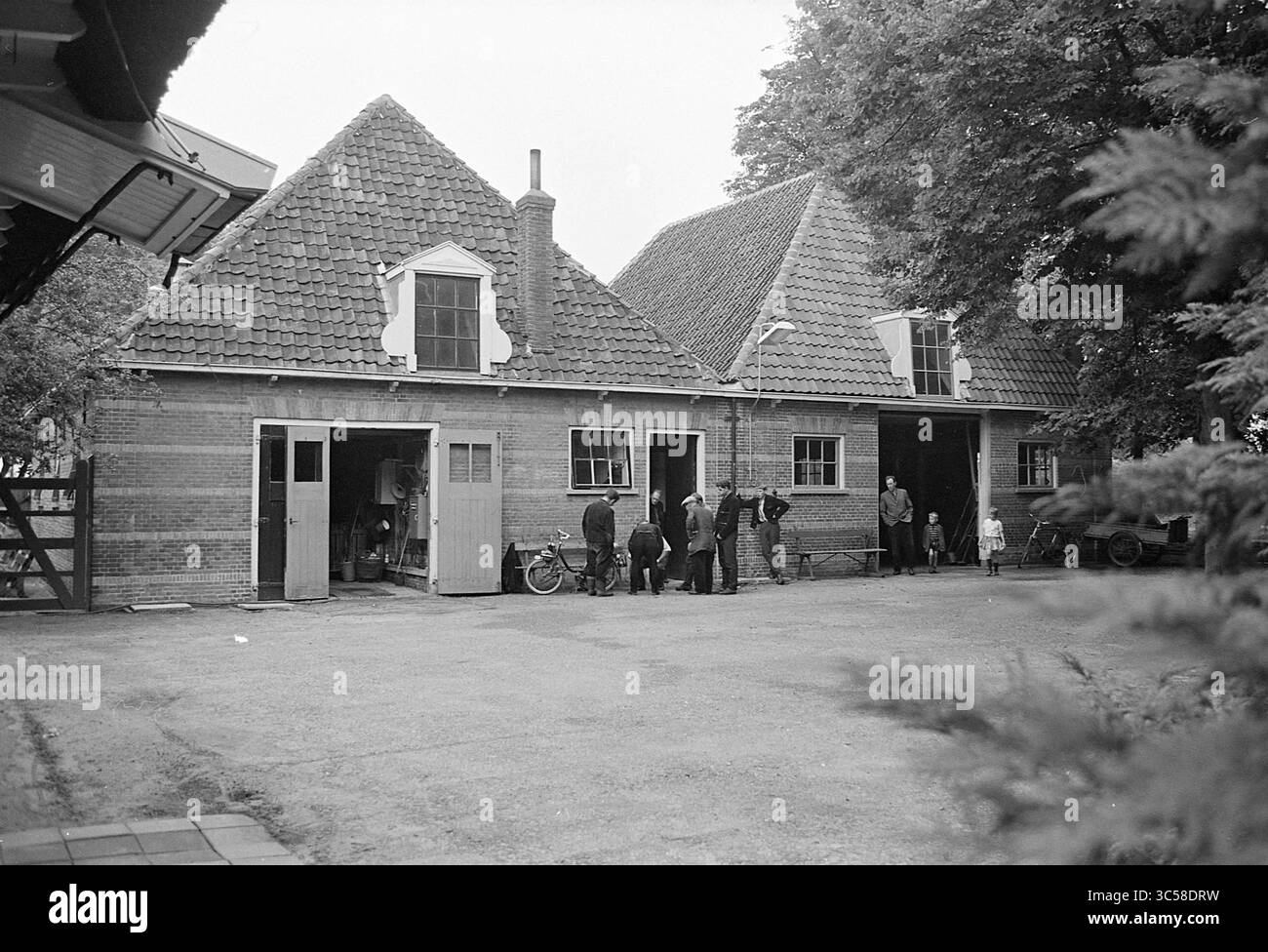 Vecchia scuola di equitazione a Velserbroek, costruzione di case e case, 20-07-1966 Whizgle News, Dutch Desk, Paesi Bassi, 1950-2000 Un gruppo di persone si è riunito di fronte a una tradizionale fattoria in stile olandese, con caratteristici tetti a spiovente e porte in legno. Le biciclette sono parcheggiate nelle vicinanze e alberi lussureggianti fanno da sfondo alla scena. Foto Stock
