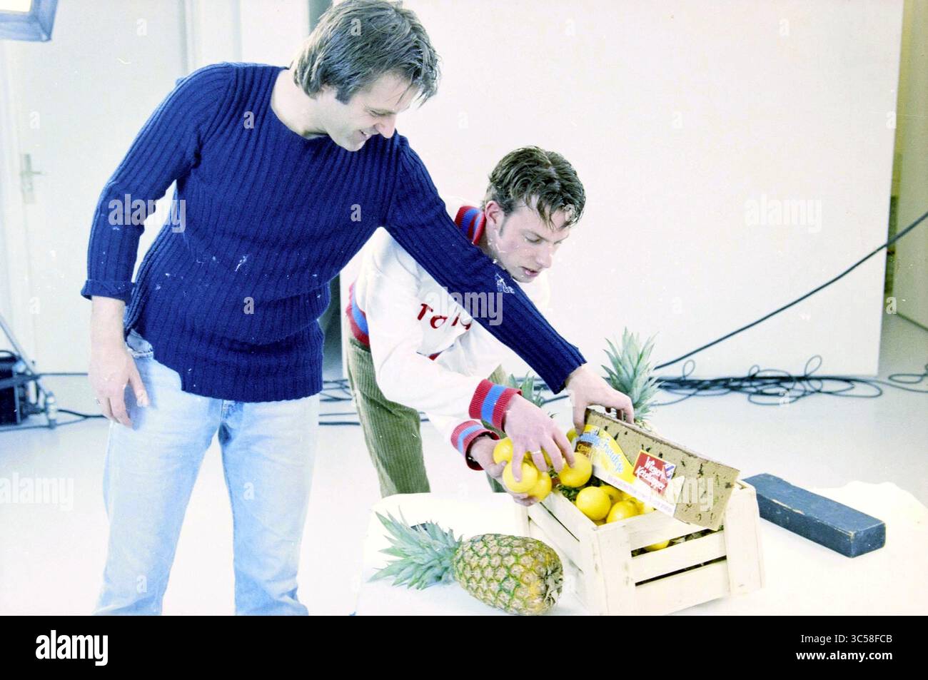 Making of 'Fruitige Froukje' Amsterdam, Amsterdam, Paesi Bassi, 16-04-2003 Whizgle News, Dutch Desk, i Paesi Bassi, 1950-2000 due persone sono impegnate a organizzare una varietà di frutta, tra cui limoni e ananas, da una cassa di legno su un tavolo, mostrando un'atmosfera giocosa e informale. Foto Stock