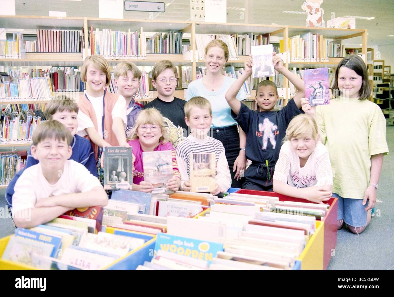 Giuria di libri per bambini, biblioteca IJmuiden, IJmuiden, Dudokplein, Paesi Bassi, 19-05-1997 Whizgle News, Dutch Desk, Paesi Bassi, 1950-2000 Un gruppo di bambini posa felicemente in una biblioteca, tenendo i loro libri preferiti. Sorrisi brillanti e una varietà di copertine di libri mostrano il loro entusiasmo per la lettura. Sullo sfondo, gli scaffali sono pieni di numerosi titoli, creando un'atmosfera vibrante di apprendimento e scoperta. Foto Stock