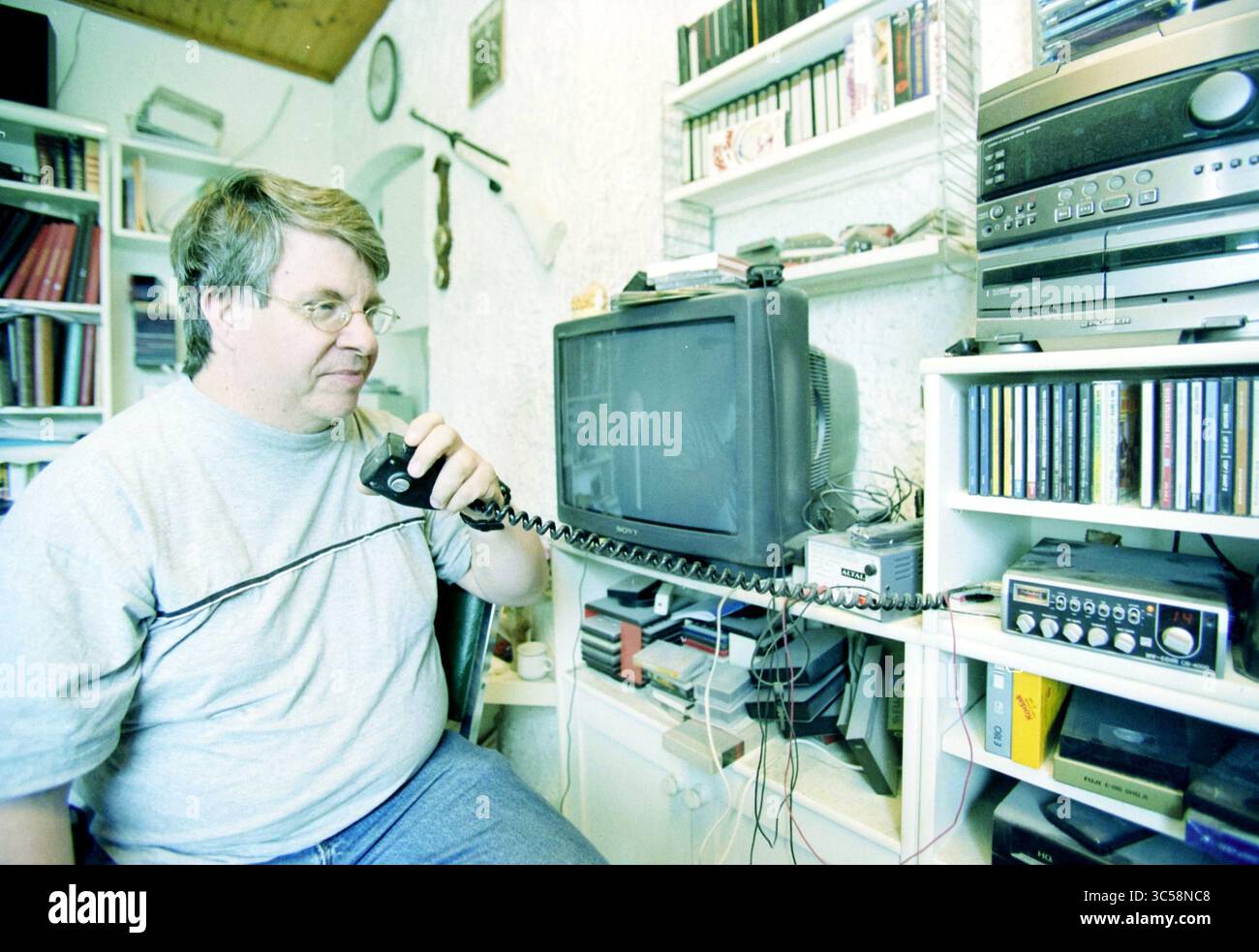 Dirk Gnobbe, IJmuiden, IJmuiden, Paesi Bassi, 11-06-2003 Whizgle News, Dutch Desk, Paesi Bassi, 1950-2000 Un uomo siede a una scrivania, impegnato in una conversazione su un telefono fisso. Intorno a lui ci sono scaffali pieni di vari libri e CD, insieme a una televisione vintage e un sistema stereo. La camera riflette un'atmosfera intima e vissuta. Foto Stock