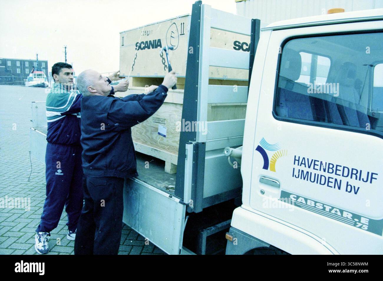 Abbigliamento Morocco, IJmuiden, IJmuiden, Paesi Bassi, 28-11-1999 Whizgle News, Dutch Desk, Paesi Bassi, 1950-2000 due persone stanno fissando una cassa di legno etichettata "SCANIA" su un veicolo, possibilmente presso una struttura di spedizione o logistica. La scena suggerisce un'attenzione particolare alla movimentazione e al trasporto delle merci. Foto Stock