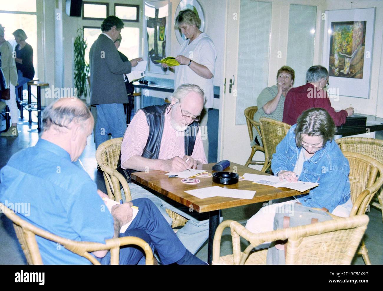 Festival in un atto, Witte Theater, IJmuiden, IJmuiden, Paesi Bassi, 25-05-1999 Whizgle News, Dutch Desk, Paesi Bassi, 1950-2000 Un accogliente spazio di ritrovo pieno di persone impegnate in varie attività. A un tavolo centrale, due individui sono concentrati sulla scrittura o sul disegno, mentre altri lavorano, chiacchierano o navigano nelle vicinanze. L'atmosfera trasuda un senso di comunità e creatività. Foto Stock