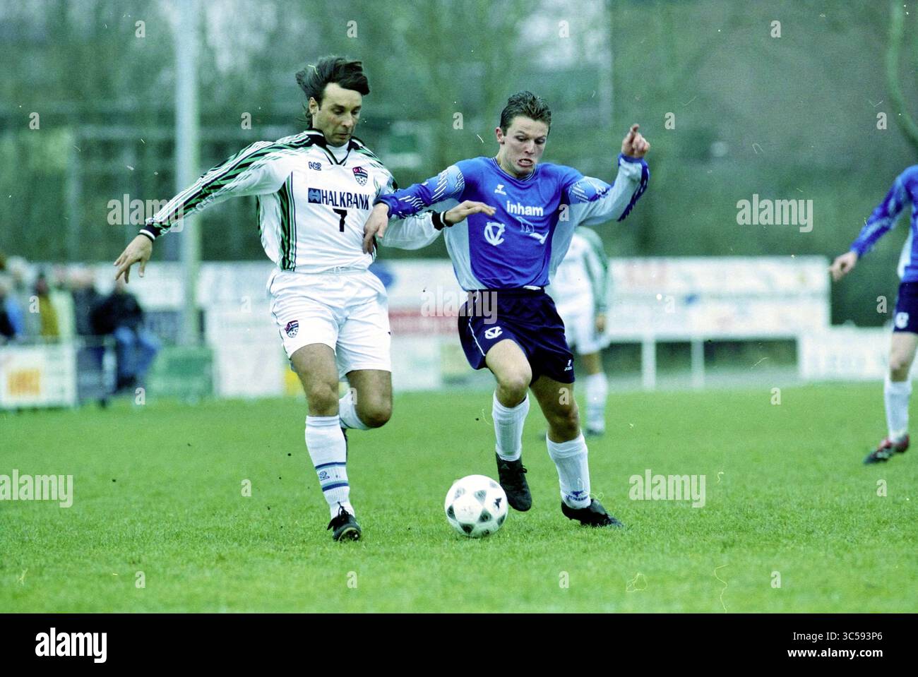 Football, Fulmars - Türkiyemspor, 10-02-2001 Whizgle News, Dutch Desk, Paesi Bassi, 1950-2000 due giocatori di calcio sono impegnati in una partita intensa, lottando per il controllo della palla su un campo erboso. Un giocatore che indossa una maglia bianca con accenti verdi difende da vicino il suo avversario, vestito con una maglia blu. La determinazione è evidente sui loro volti mentre si sforzano di superarsi a vicenda. Foto Stock