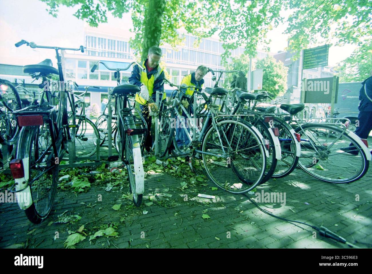 Relitti di biciclette alla stazione di Haarlem, Haarlem, Paesi Bassi, 11-07-2000 Whizgle News, Dutch Desk, i Paesi Bassi, 1950-2000 due persone in giubbotti luminosi stanno organizzando un gruppo di biciclette in mezzo a foglie cadute, con uno sfondo di edifici moderni e verde. Foto Stock