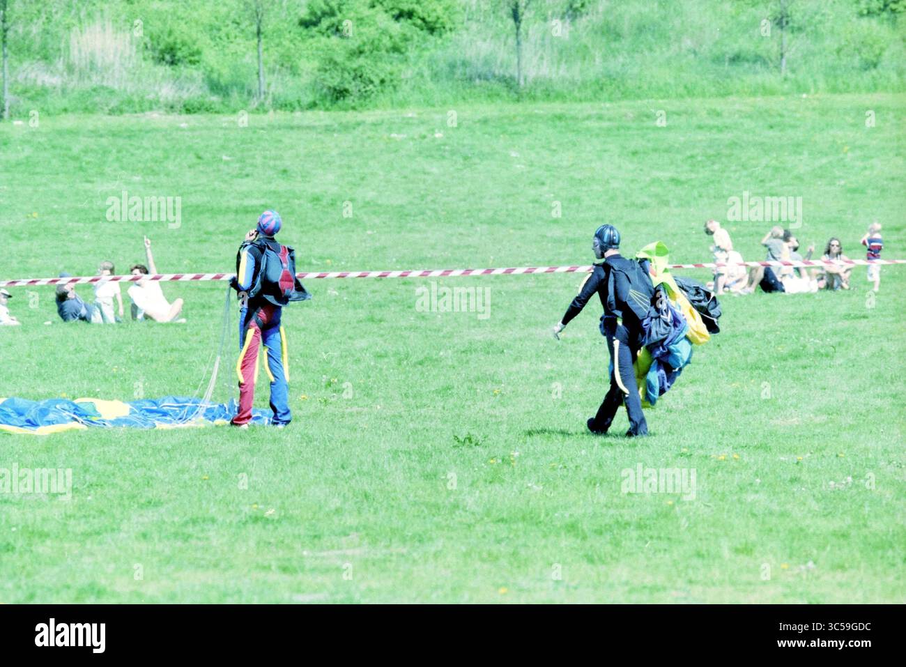 Dimostrazione di paracadute, Spaarnwoude, Spaarnwoude, 06-05-2000 Whizgle News, scrivania olandese, i Paesi Bassi, 1950-2000 due persone con attrezzatura da paracadutismo acrobatico camminano su un campo erboso, preparandosi per un salto, mentre un gruppo di persone si rilassa sullo sfondo, godendosi una giornata di sole. Foto Stock