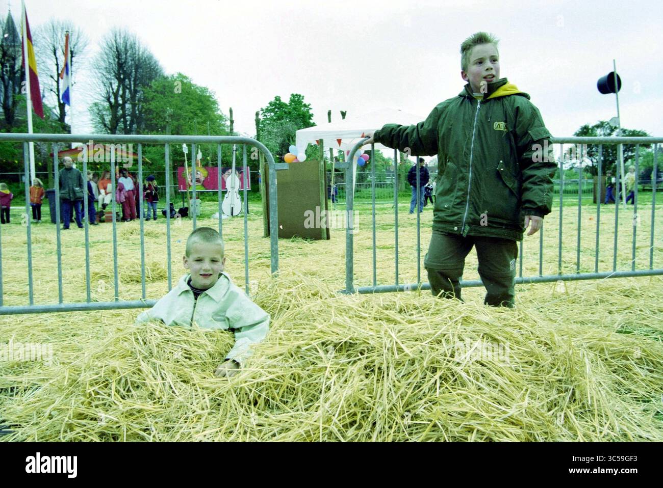 Queen's Day Event@@, Bennebroek, Bennebroek, 28-04-2000 Whizgle News, scrivania olandese, i Paesi Bassi, 1950-2000 due bambini giocano in un'area piena di paglia in un evento all'aperto. Un bambino è seduto tra la paglia, mentre l'altro si trova nelle vicinanze, entrambi sembrano allegri e impegnati nel loro ambiente giocoso. Sullo sfondo, una scena vivace si svolge con varie attività e persone che si godono i festeggiamenti. Foto Stock
