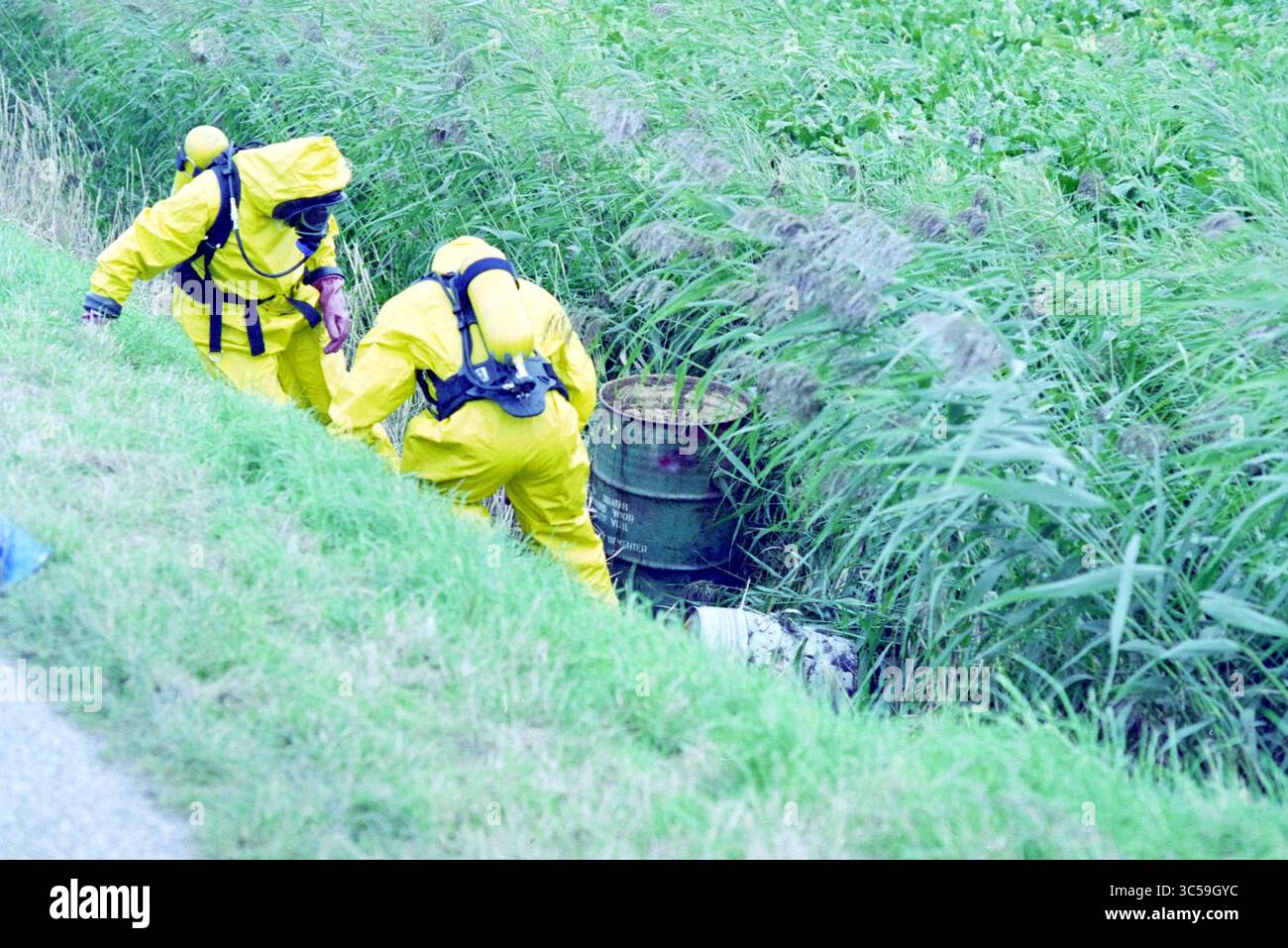 Scoperta di botti di veleno a Spaarnwoude, Spaarnwoude, 02-10-1995 Whizgle News, Dutch Desk, Paesi Bassi, 1950-2000 due persone in tute protettive brillanti stanno indagando su un barile vicino a un'area erbosa. Sembrano concentrati sul loro compito, circondati da una fitta vegetazione. Foto Stock