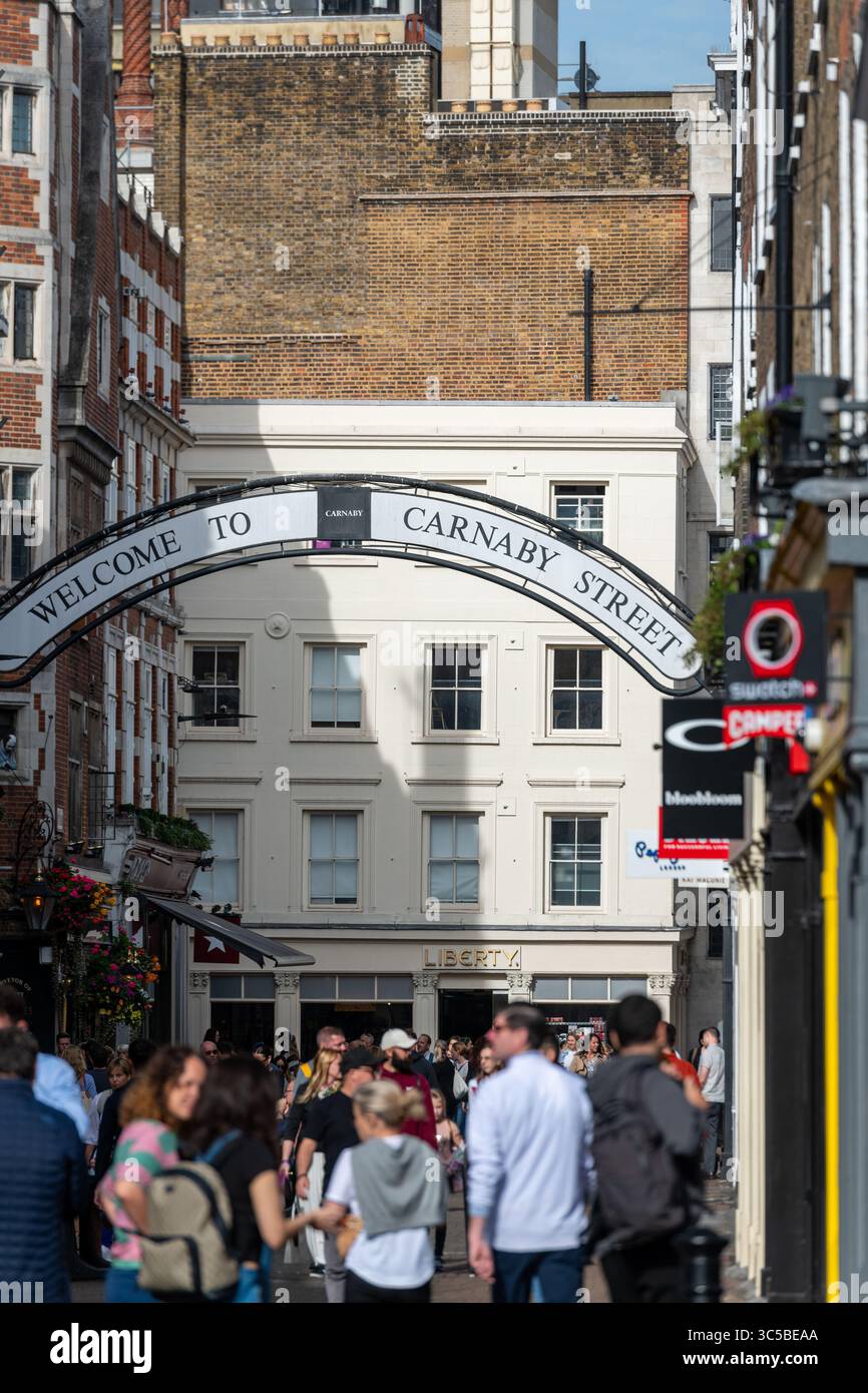 I turisti e gli amanti dello shopping camminano sotto l'iconico cartello Welcome to Carnaby Street in un'intensa giornata estiva nel quartiere di Soho a Londra Foto Stock