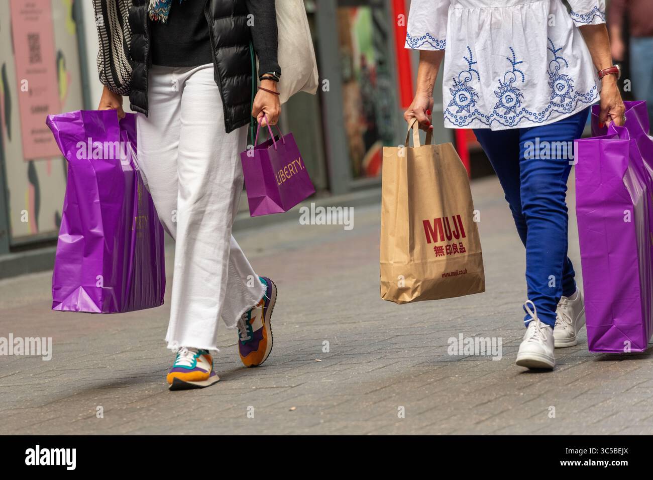 Gli amanti dello shopping camminano con Liberty London e le borse MUJI su Carnaby Street, una popolare destinazione di vendita al dettaglio a Soho, Londra, Regno Unito. Foto Stock