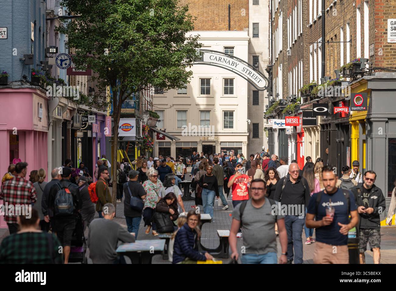 Carnaby Street, nel West End di Londra, è affollata di persone che fanno shopping e camminano sotto l'iconico cartello stradale in un pomeriggio estivo. Foto Stock