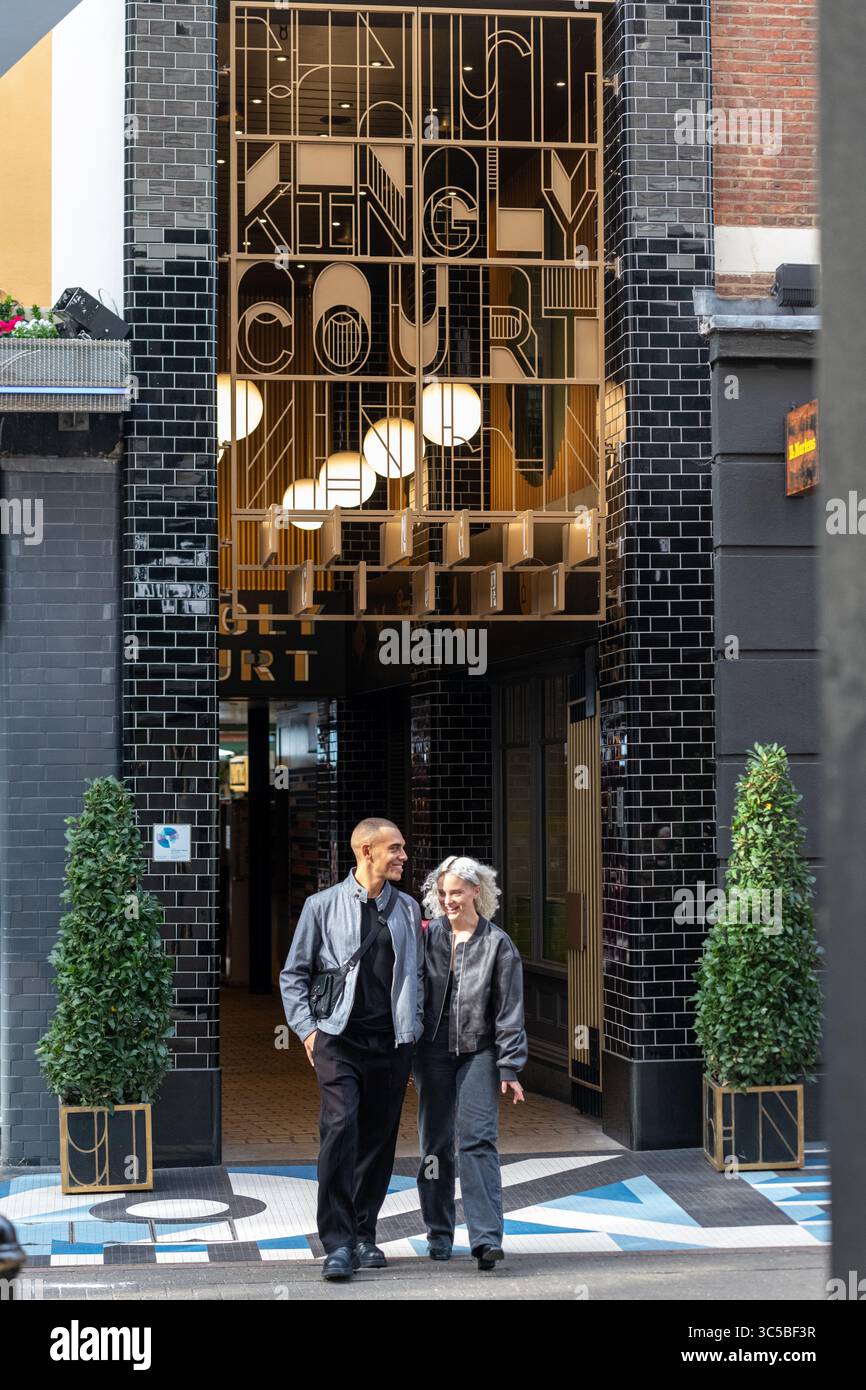Una coppia passeggia davanti all'ingresso di Kingly Court, una popolare destinazione per lo shopping e i ristoranti a Soho, Londra, Inghilterra. Foto Stock