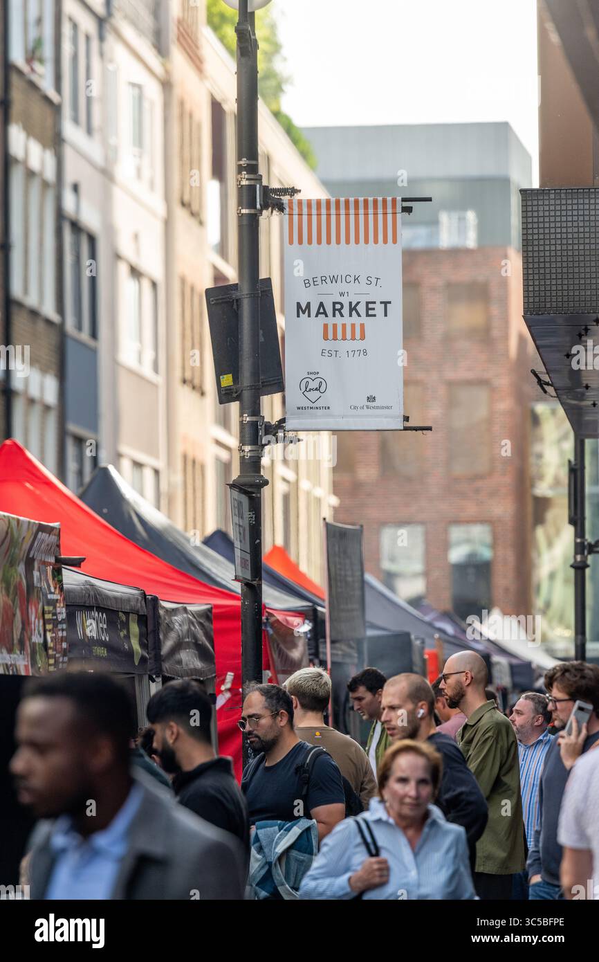 Pomeriggio intenso al mercato di Berwick Street a Soho, Londra, con folle di persone che fanno shopping e un cartello sopra la testa. Foto Stock