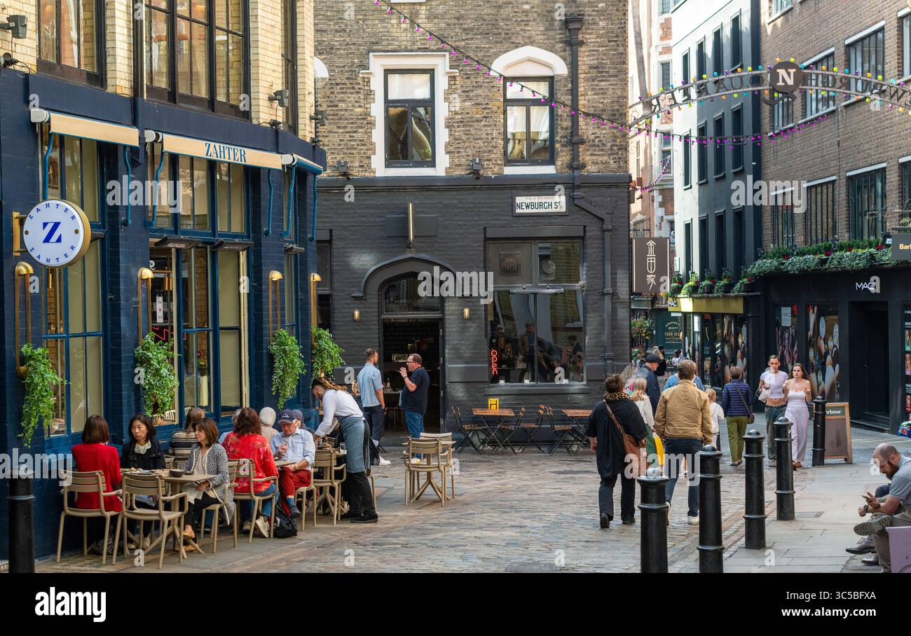 Persone che amano mangiare e bere all'aperto su Newburgh Street a Soho, Londra, con caffetterie, ristoranti e una vivace atmosfera estiva nel Carnaby A. Foto Stock
