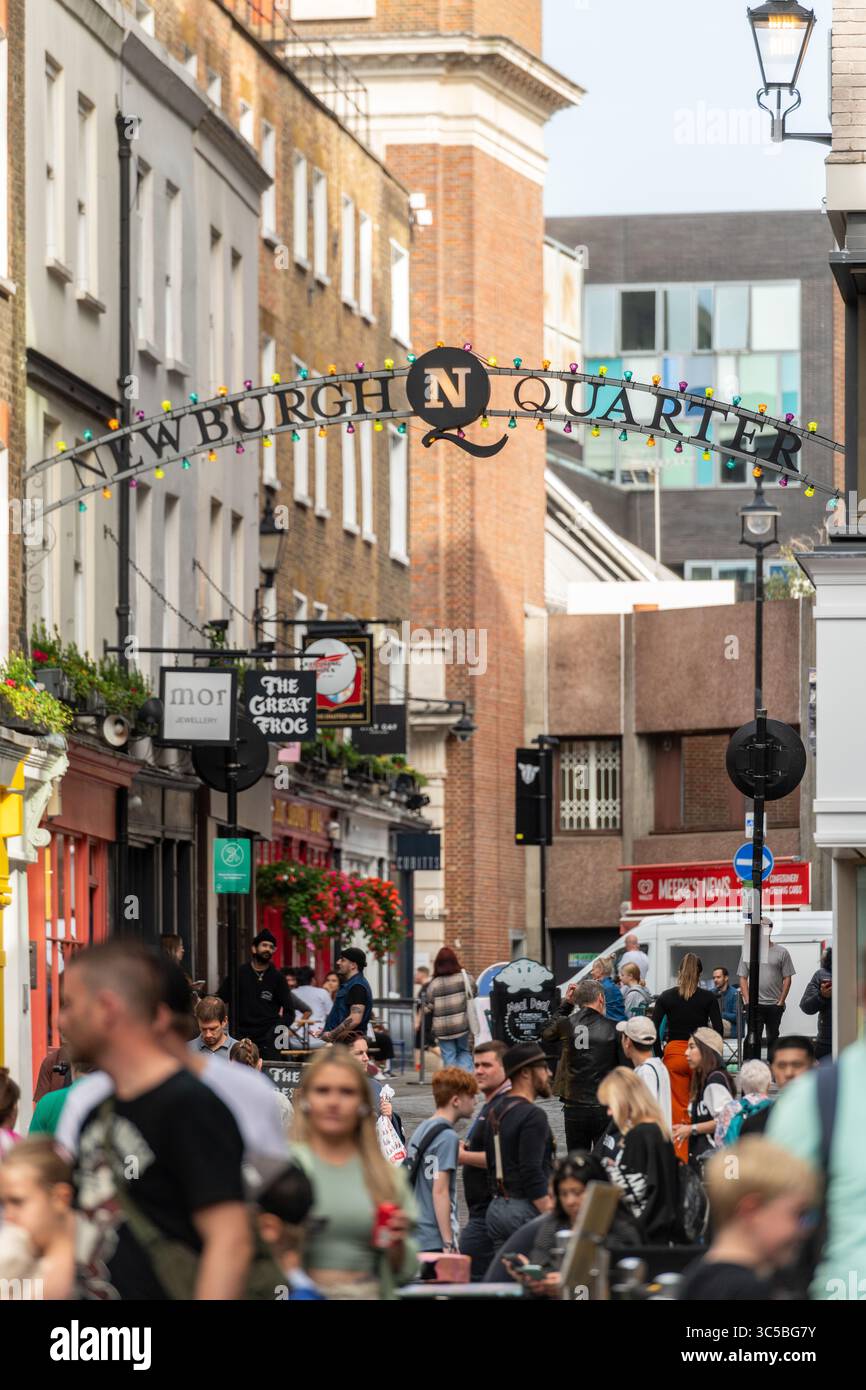 La folla passeggia sotto l'arco del quartiere di Newburgh a Soho, Londra, una popolare destinazione per lo shopping e i ristoranti nei pressi di Carnaby Street in un pomeriggio intenso. Foto Stock