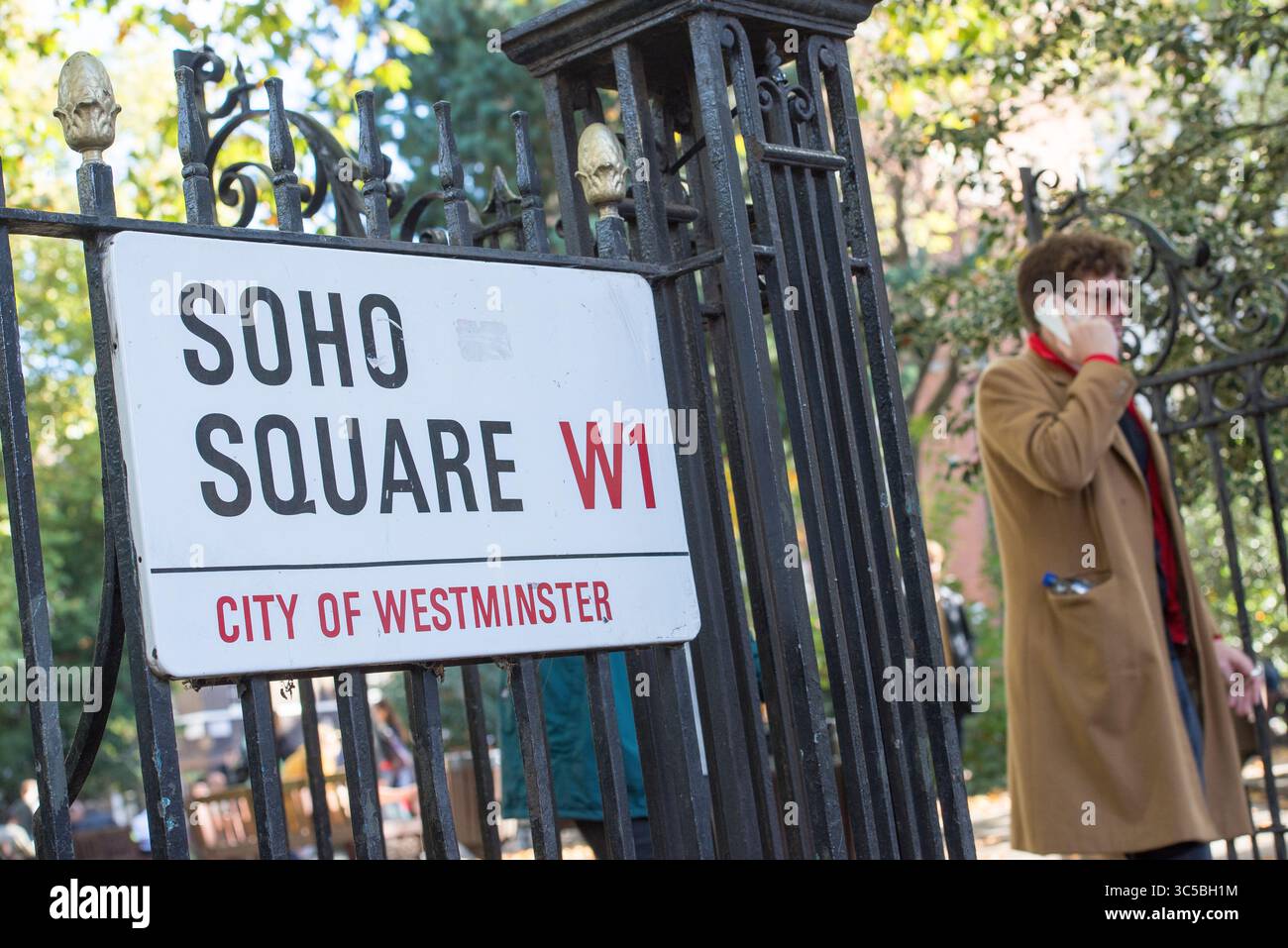 Soho Square Street sign nella City of Westminster, Londra, con un uomo al telefono che passa sullo sfondo in una giornata di sole. Foto Stock