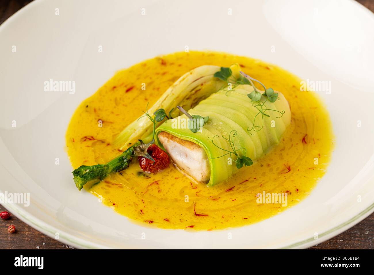 Filetto di pesce ricoperto di zucchine in salsa gialla allo zafferano Foto Stock