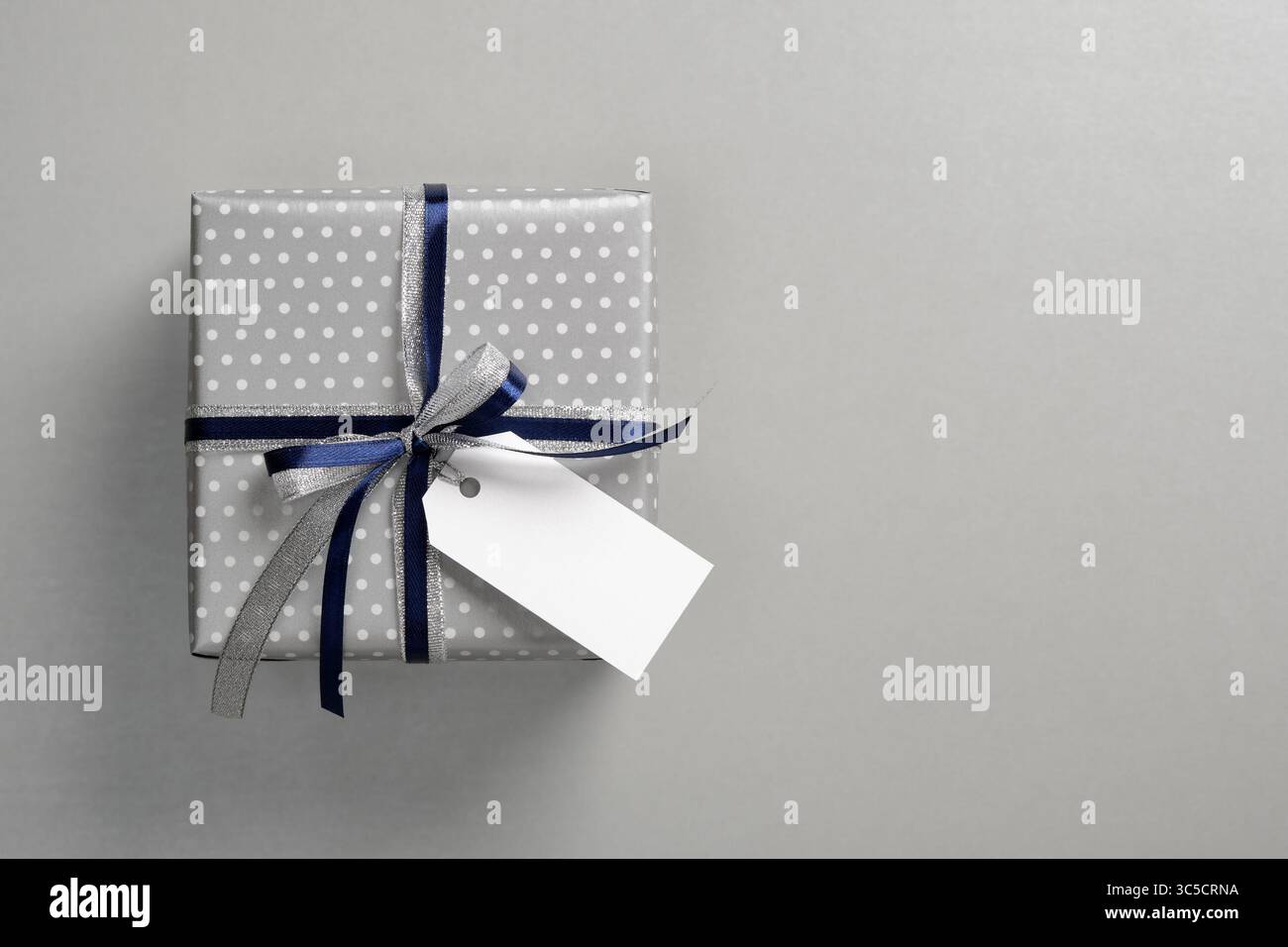 La confezione regalo è decorata con carta a pois color argento e legata con un nastro in argento lucido e blu scuro. Un'etichetta bianca vuota è appesa al fiocco per te Foto Stock