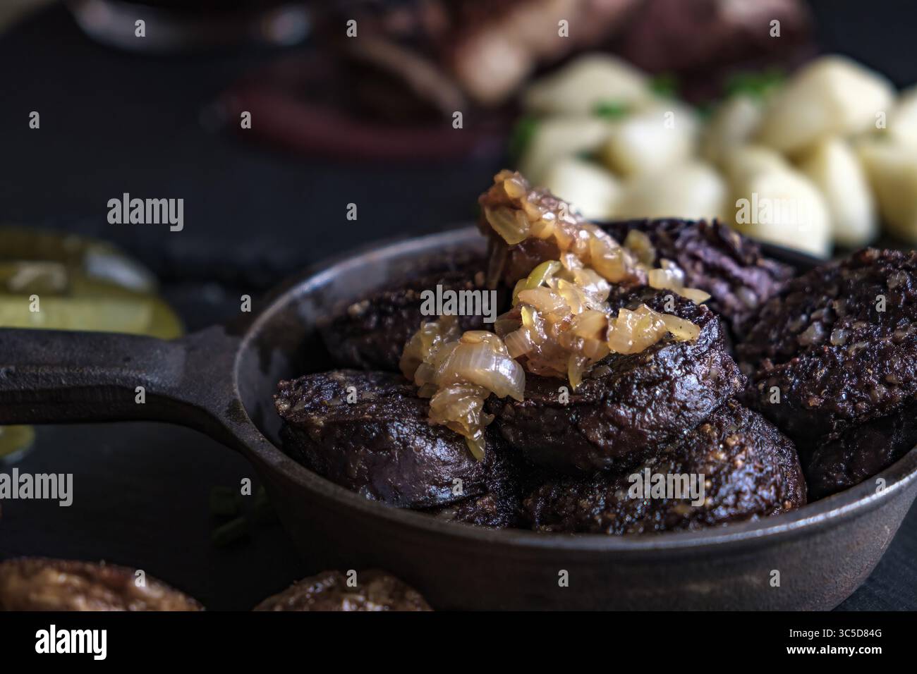 Tradizionale kaszanka polacca, un tipo di budino nero o salsiccia di sangue, servito con cipolle caramellate in una padella rustica, con gnocchi nel backgro Foto Stock