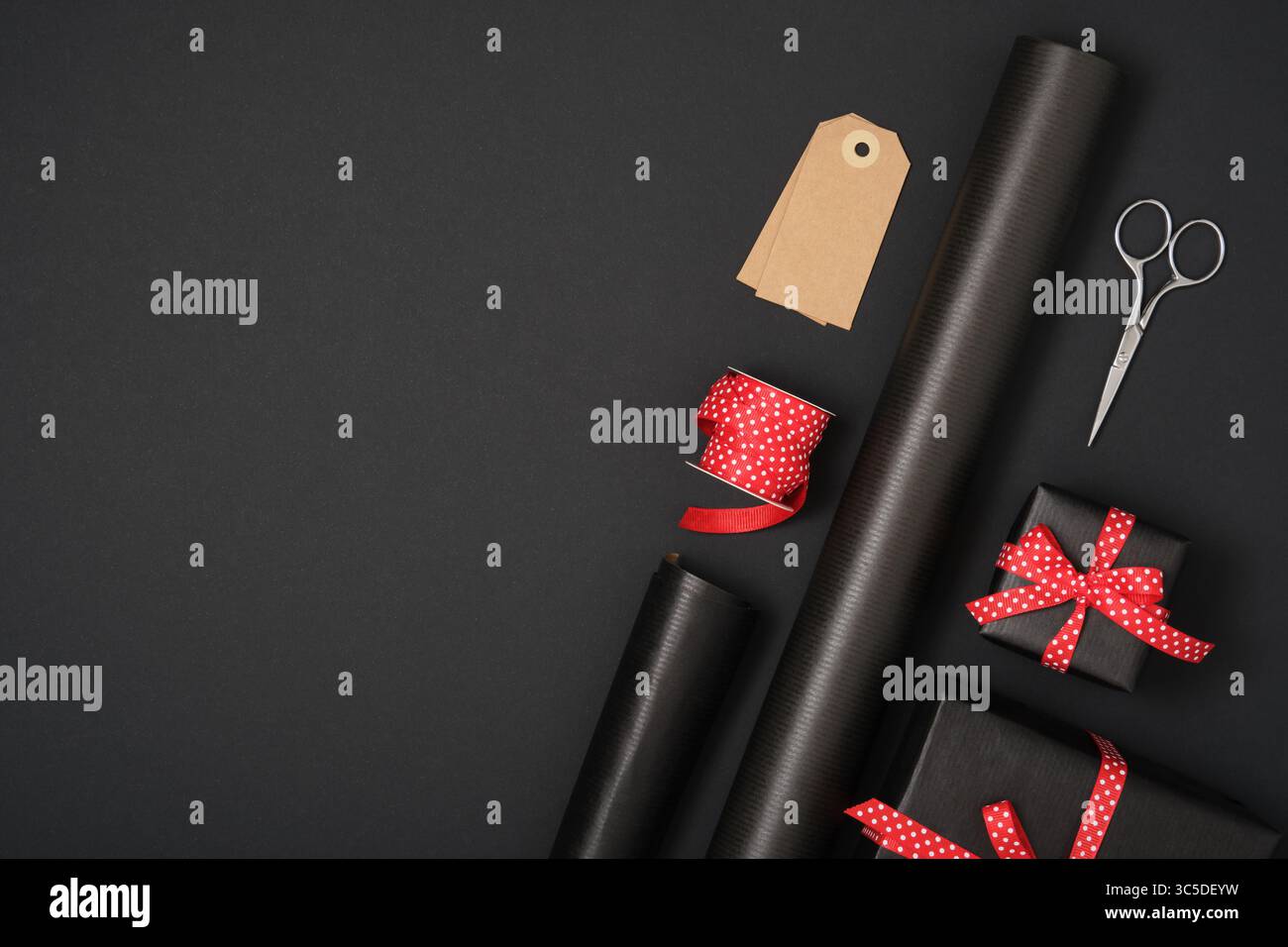 Adoro la confezione regalo. Carta da imballaggio nera, nastro rosso tratteggiato, cartellino regalo, scatola, forbici. Copyspace Foto Stock