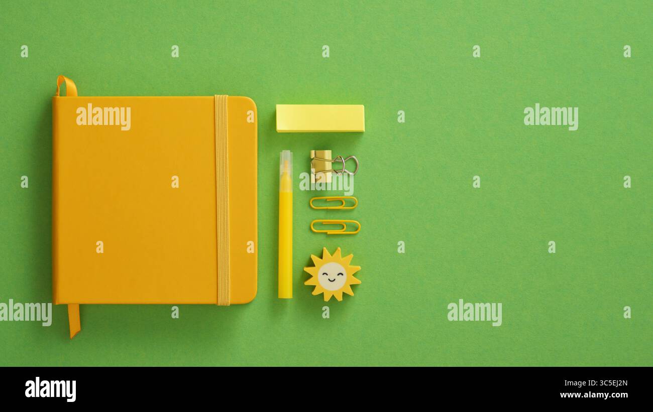 Blocco note giallo chiuso con pennarello per cancelleria, graffette, spille, adesivi su sfondo verde. Spazio per il testo. Foto Stock
