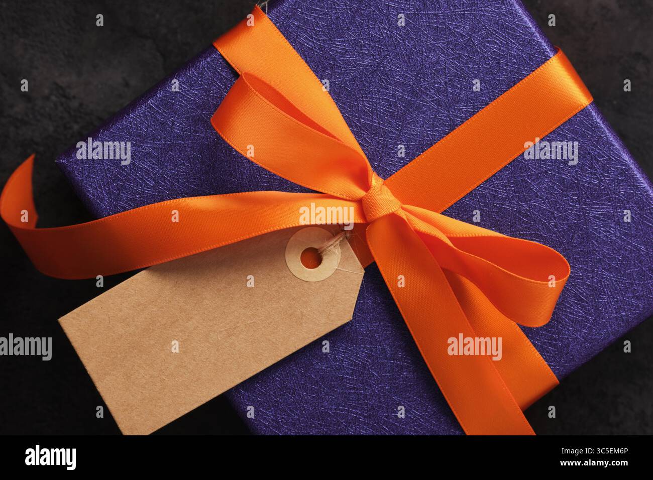 Regalo di Halloween avvolto in carta viola con nastro arancione e etichetta vuota rettangolare. Un posto per il testo Foto Stock