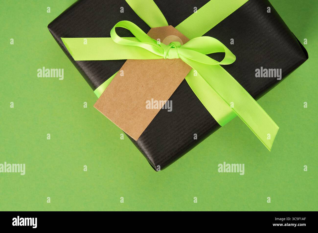 Striscione con confezione regalo nera, nastro verde neon ed etichetta vuota. Sfondo verde, spazio per il testo. Foto Stock