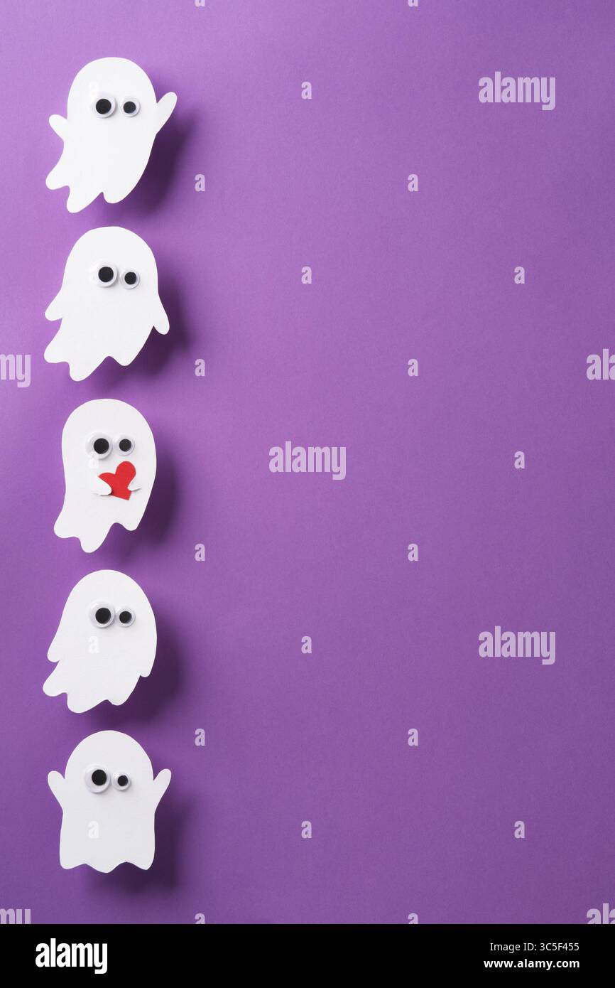 Simpatici fantasmi con occhi su sfondo viola, un fantasma con cuore rosso, banner verticale Halloween, spazio per il testo Foto Stock