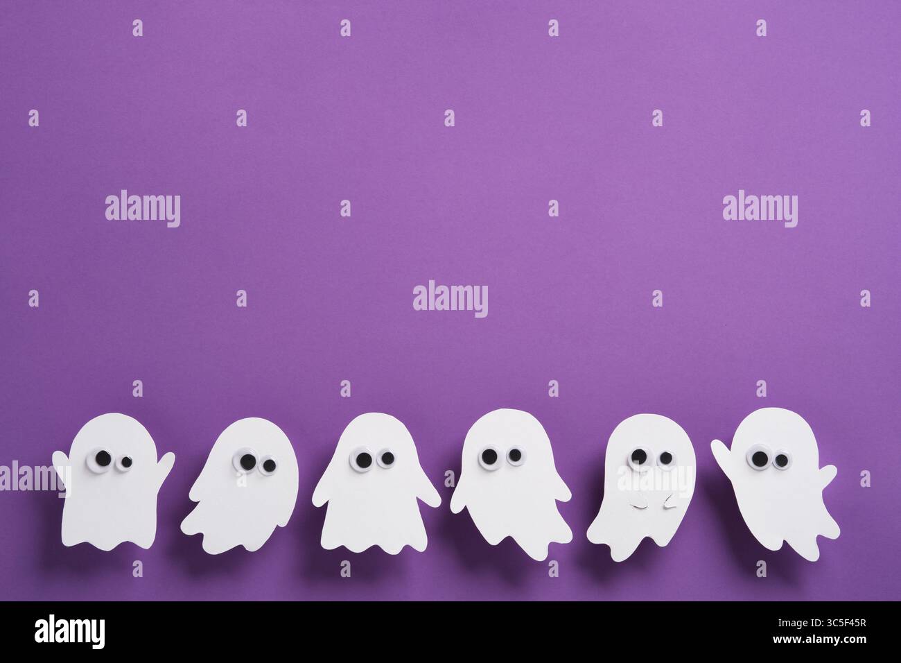 Adorabili figure fantasma bianche con occhi strani su sfondo viola, divertente e spettrale striscione di Halloween con spazio di copia Foto Stock